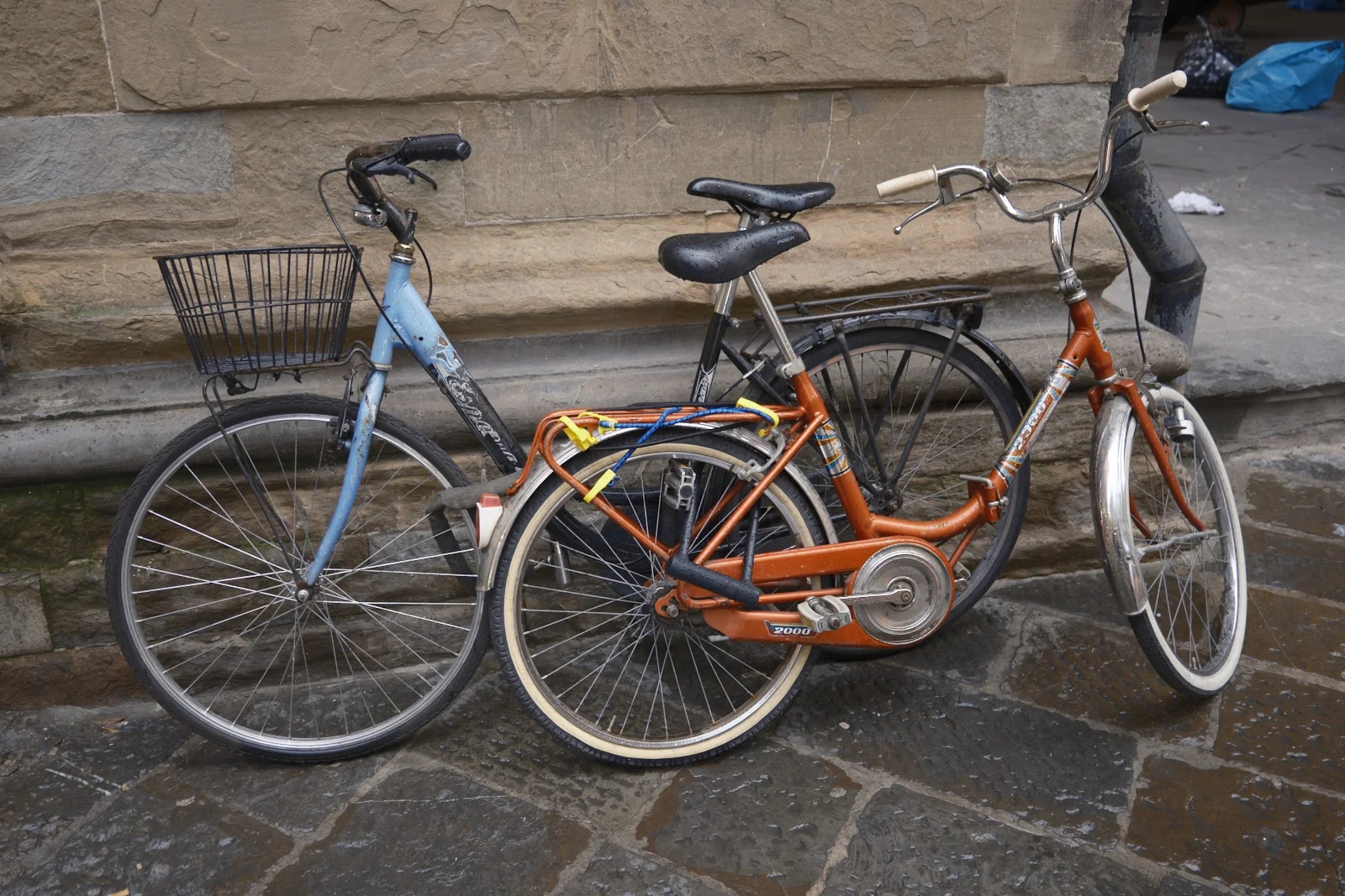 Blue and orange bicycles leaning against a stone wall
