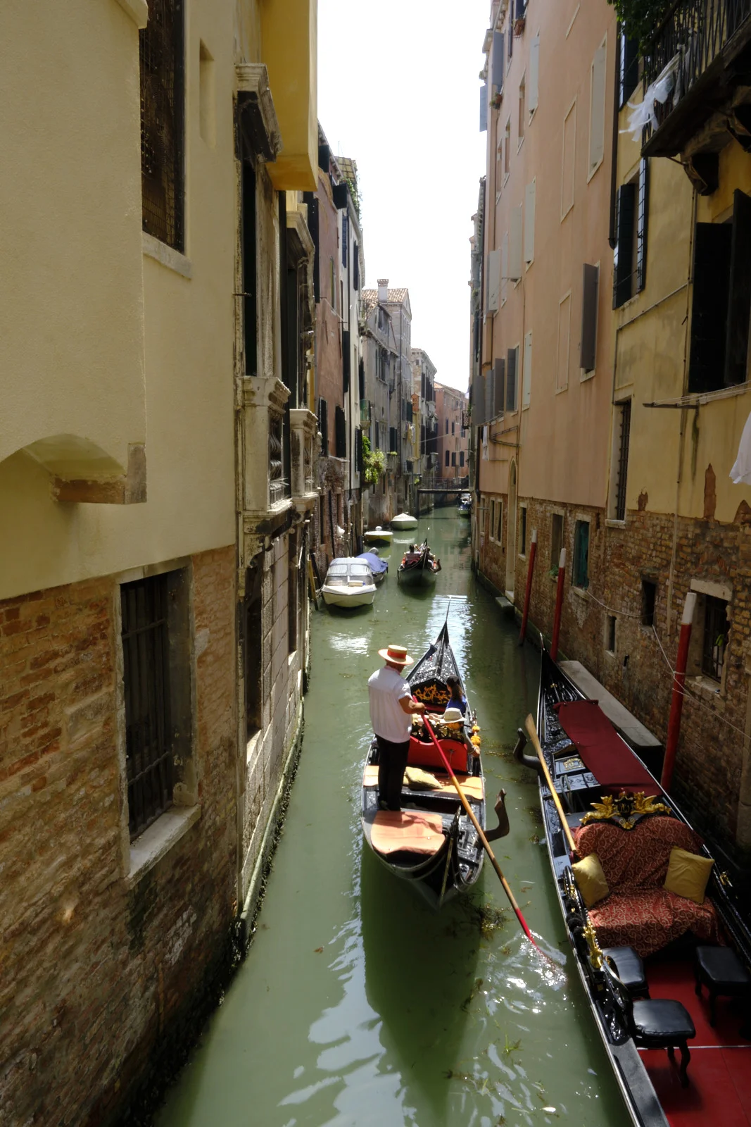 Gondolier in a straw hat poling a gondola down a narrow Venetian rio