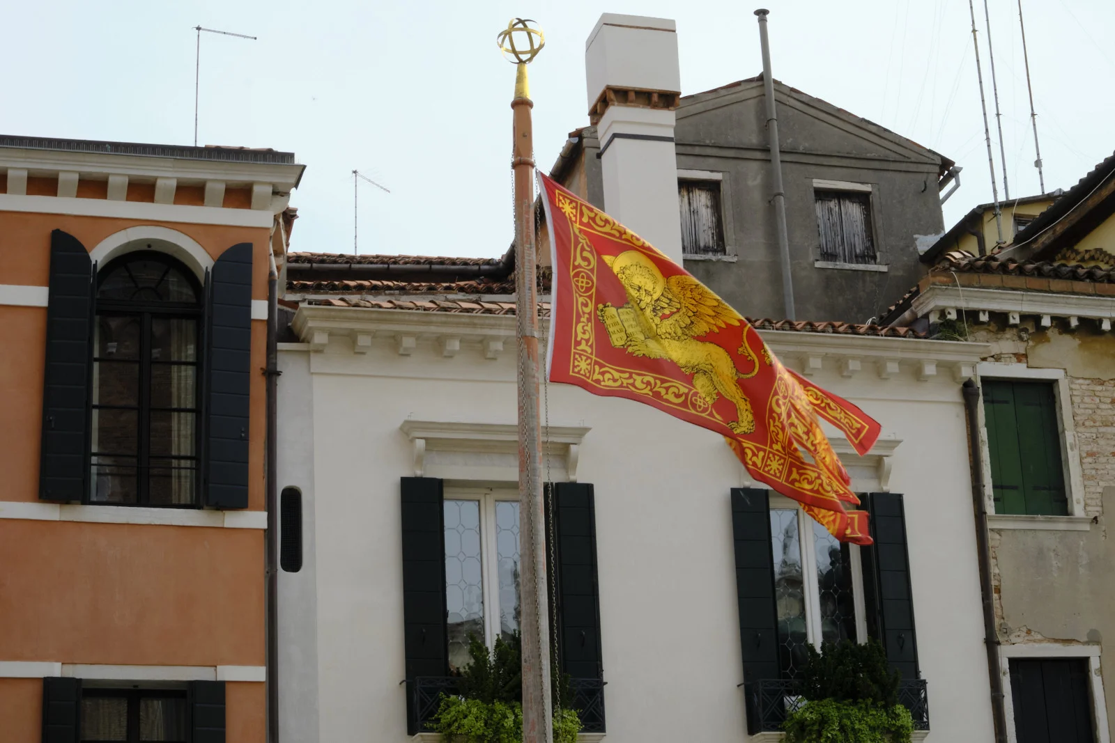 Red and gold flag of Venice with the winged lion flying before shuttered houses