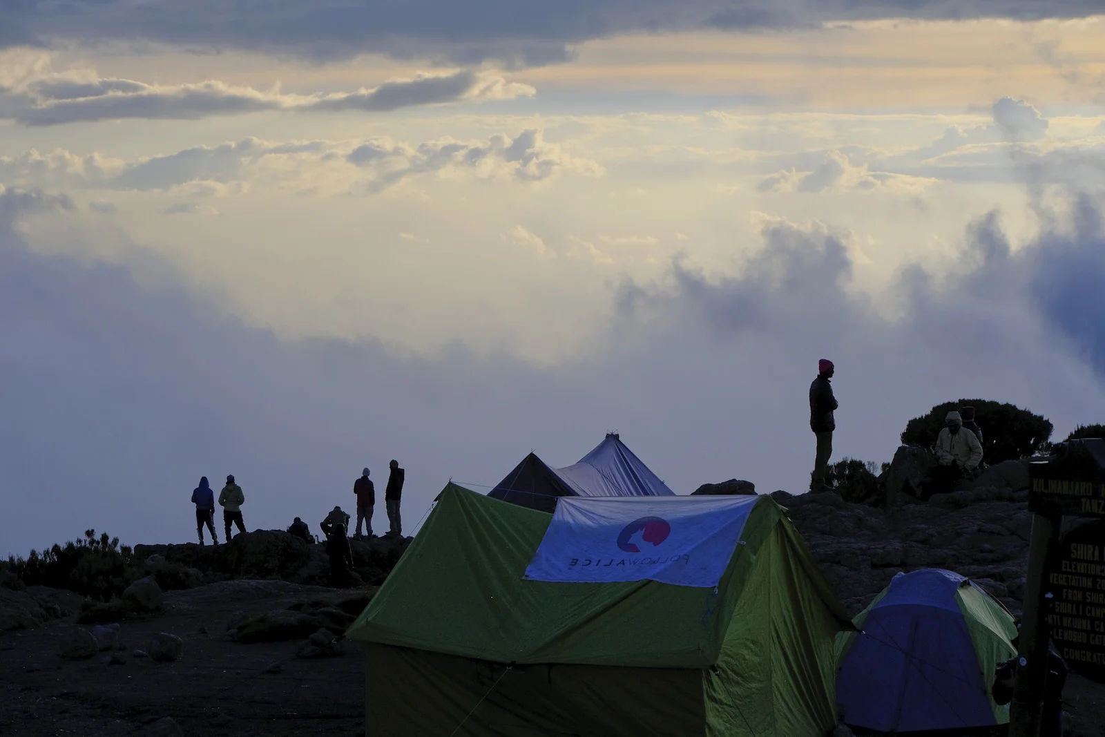 Silhouettes of tents and people against evening cloud