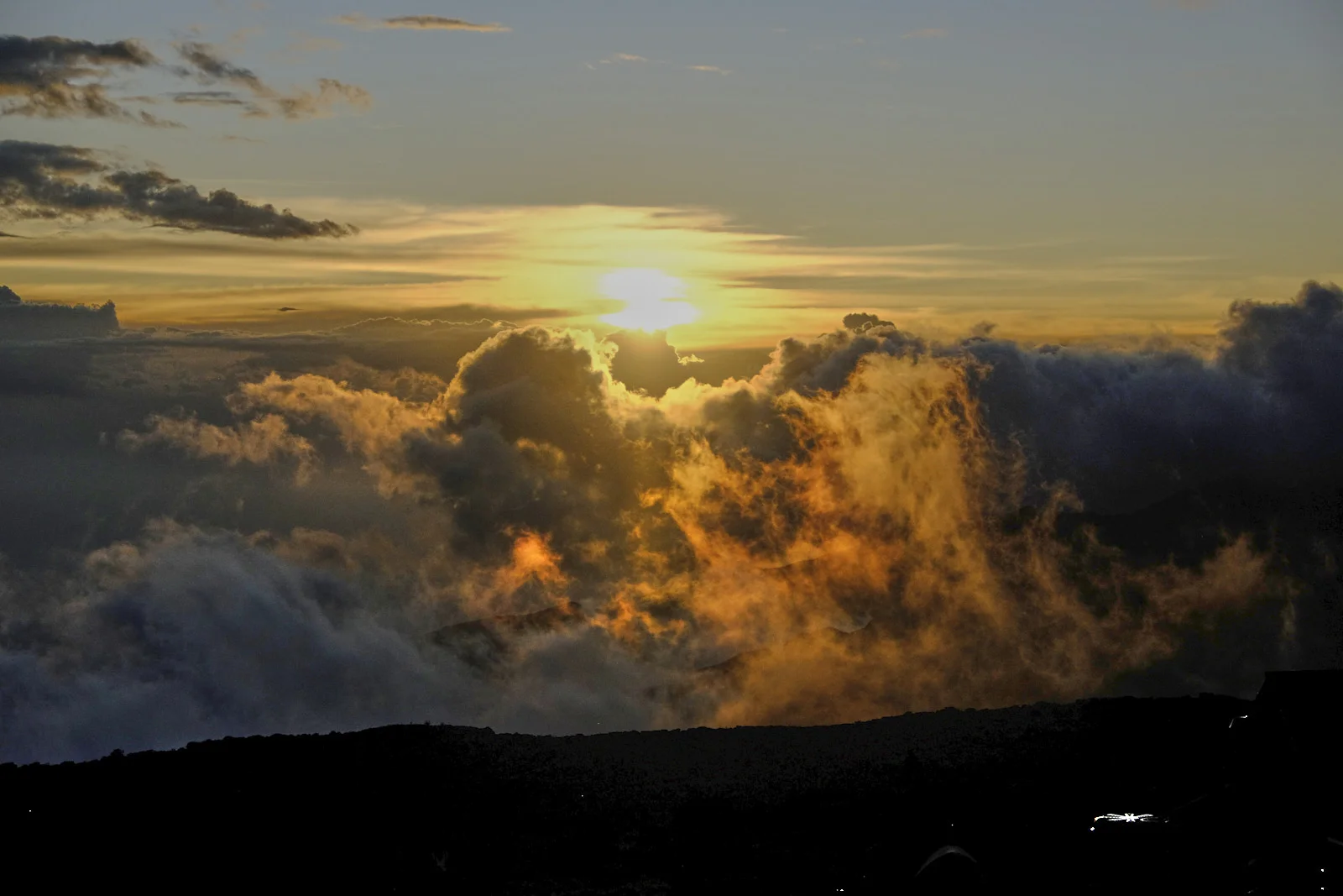 Sun breaking through cloud above a dark ridge