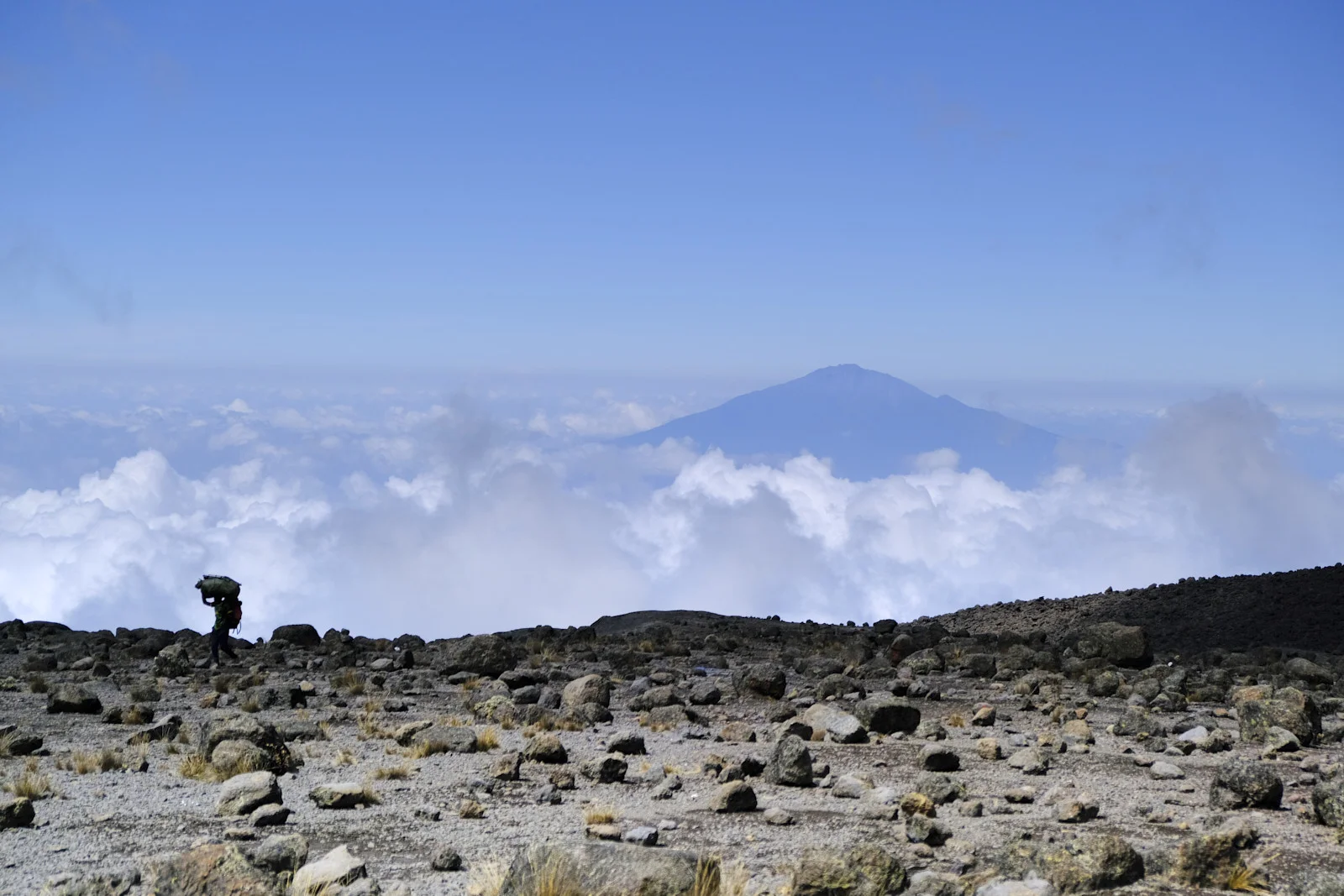 Porter on an alpine desert ridge with Mount Meru above the clouds
