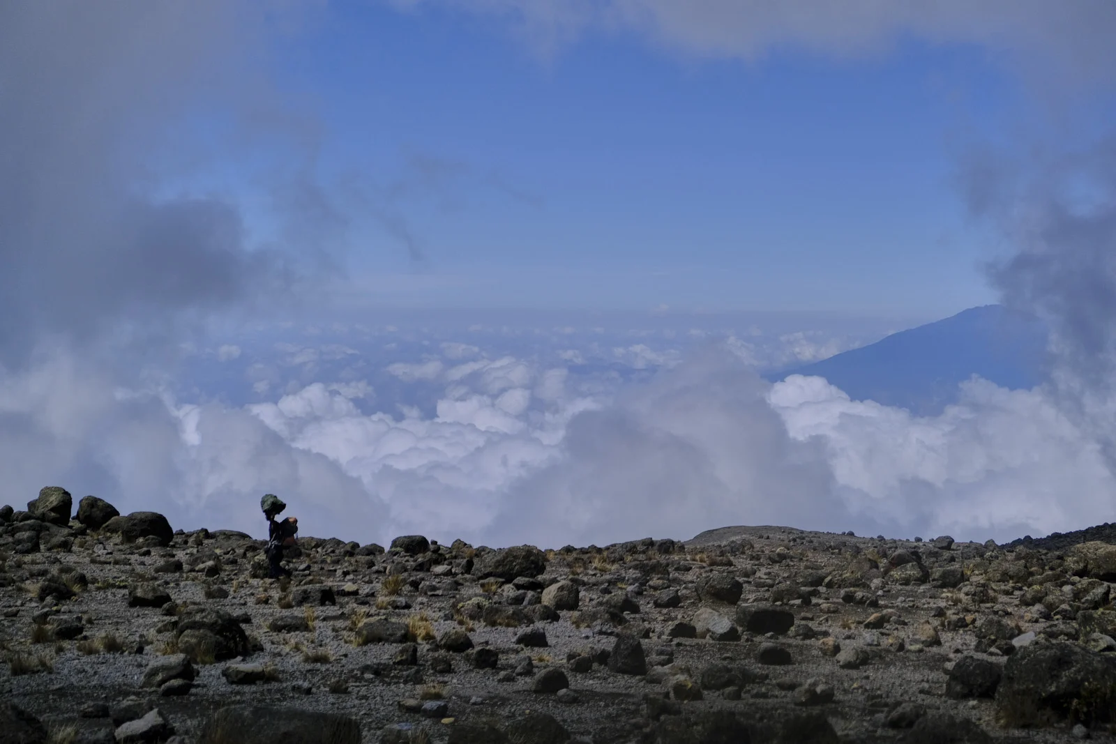 Porter with a head load on scree above a sea of cloud