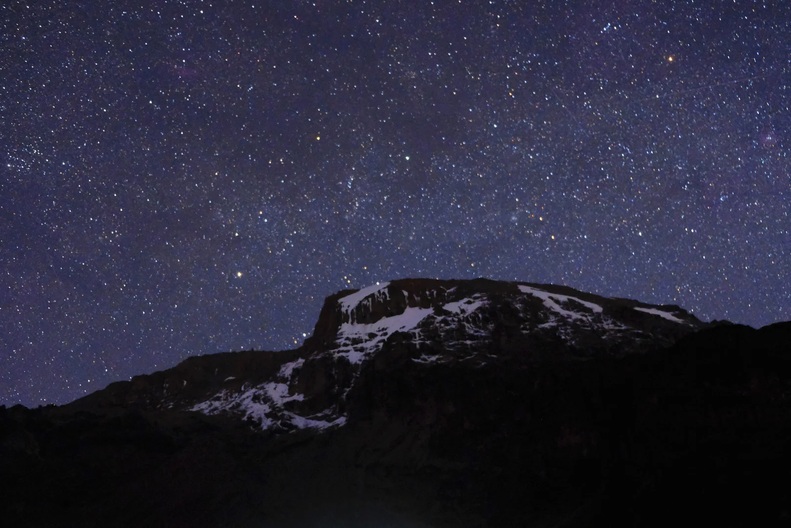 Starry sky over Kibo’s snowy cliff above camp lights