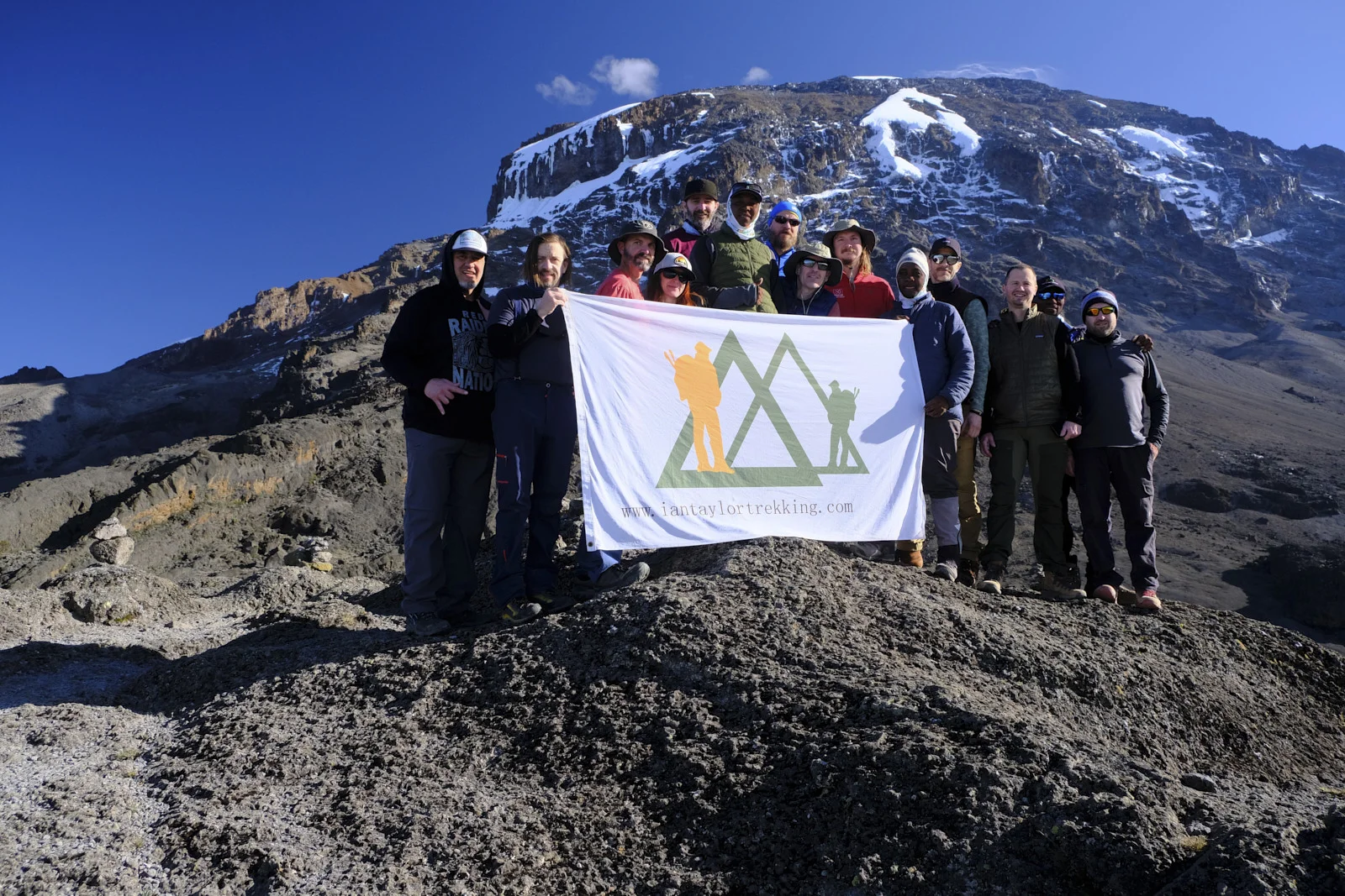 Climbing team holding an Ian Taylor Trekking banner with Kibo behind