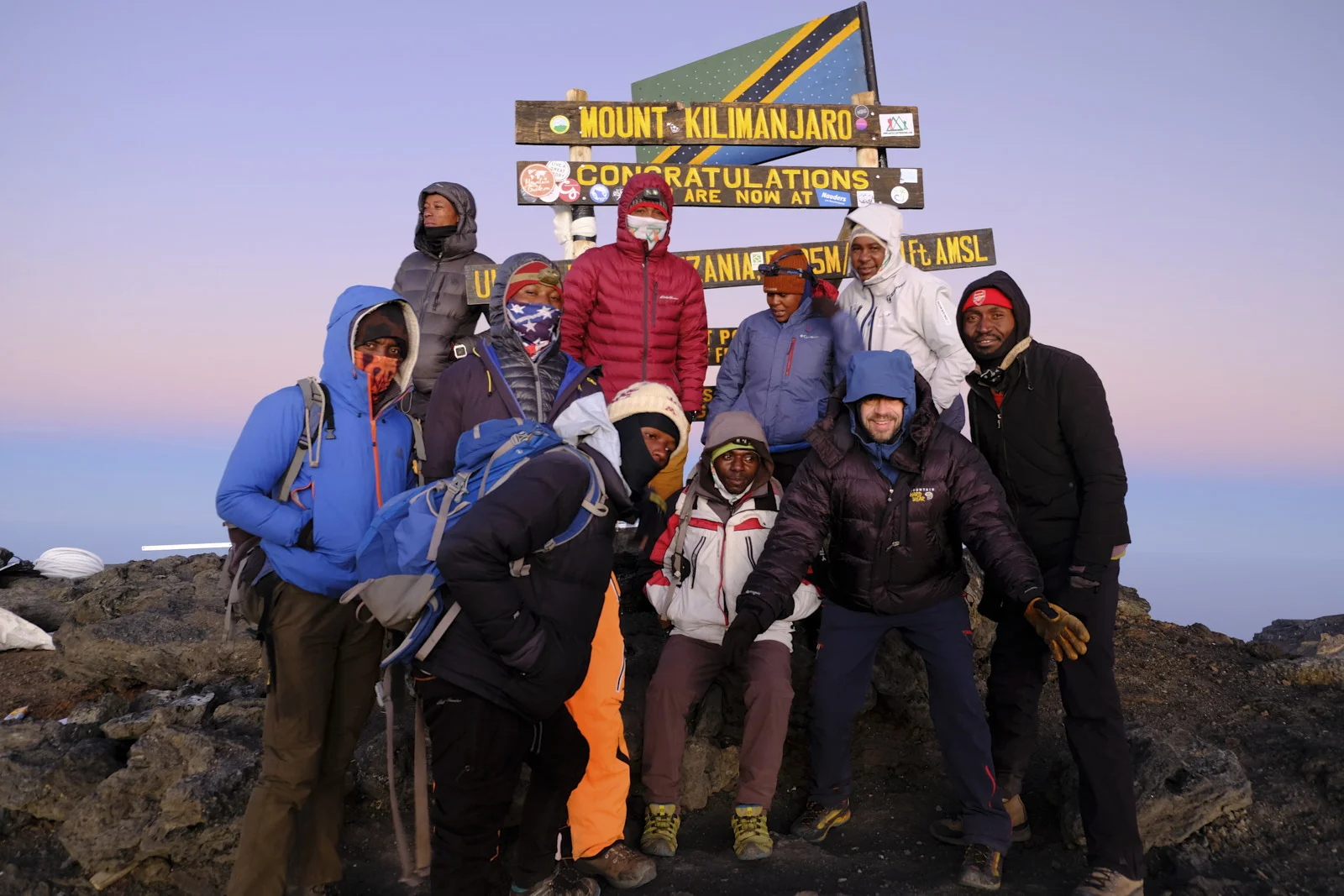 Climbing team at the Uhuru Peak sign under a Tanzanian flag
