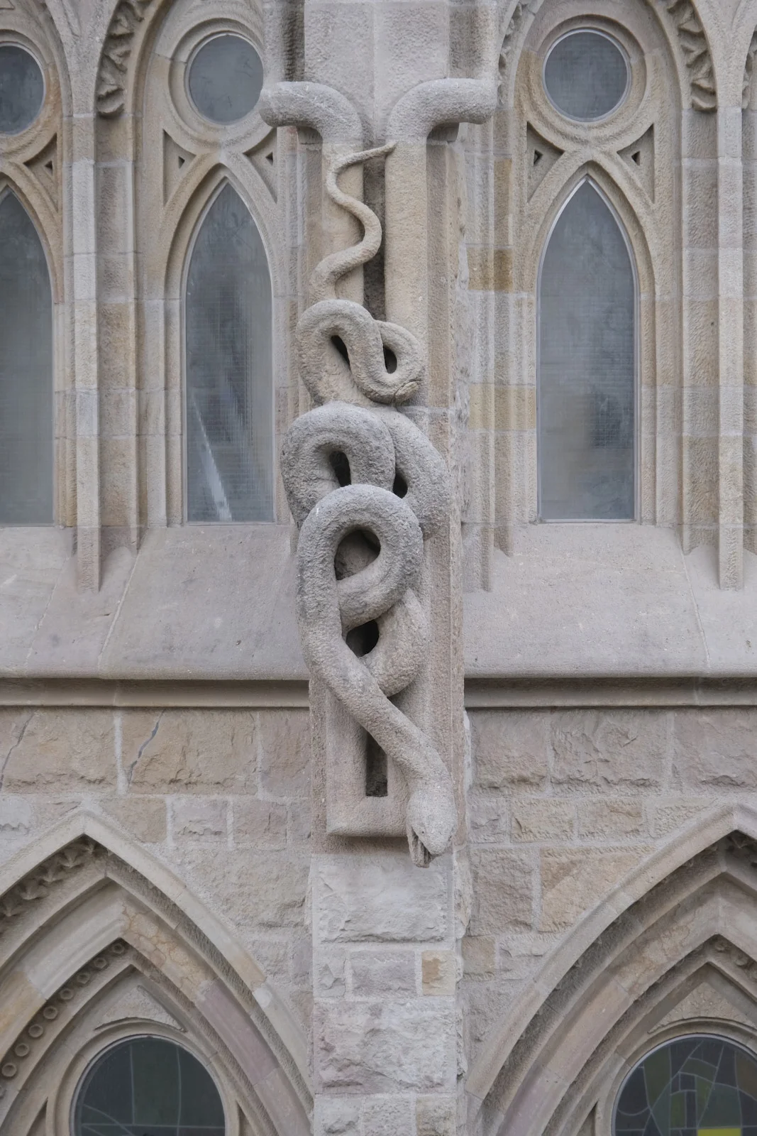 A stone serpent coiled around a column between pointed windows on the Nativity facade of the Sagrada Família in Barcelona.