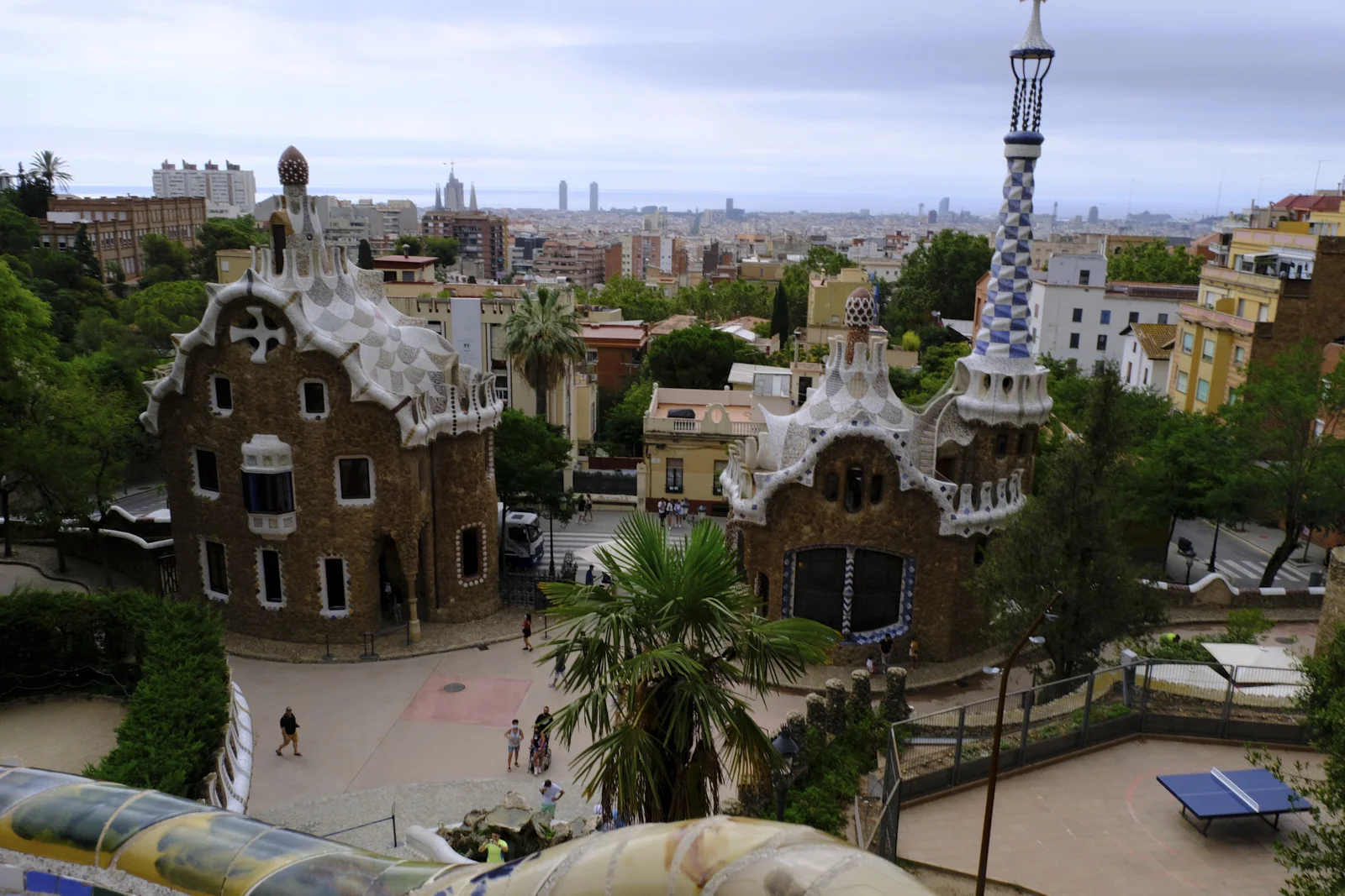 Both entrance pavilions at Park Güell in Barcelona, seen from the terrace above the street, with the city beyond.