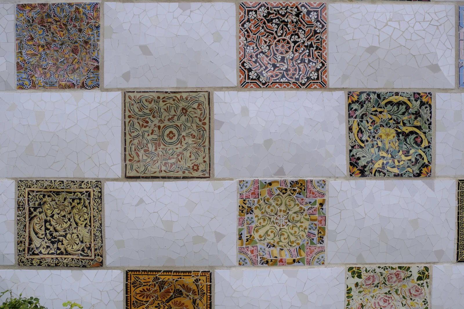 A trencadís wall beside the entrance stairway at Park Güell in Barcelona, a grid of plain tile squares and patterned ceramic panels.