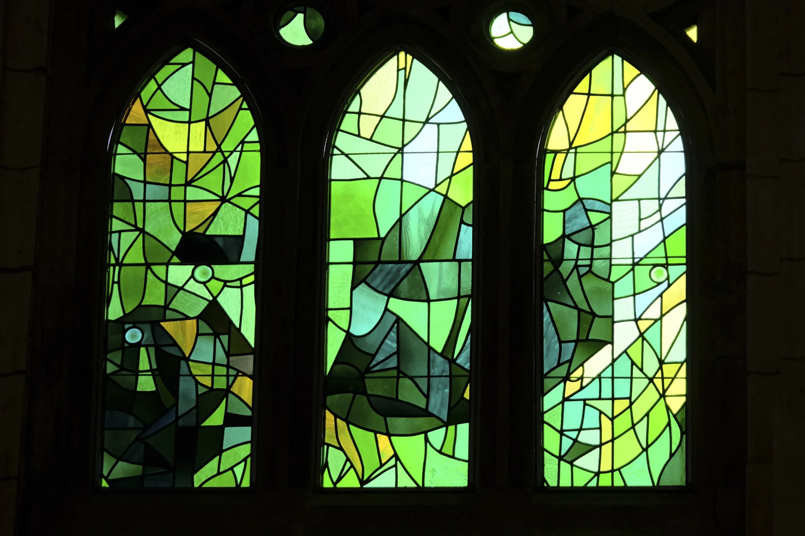 Three pointed stained-glass windows with green and yellow abstract glass in the Sagrada Família in Barcelona.