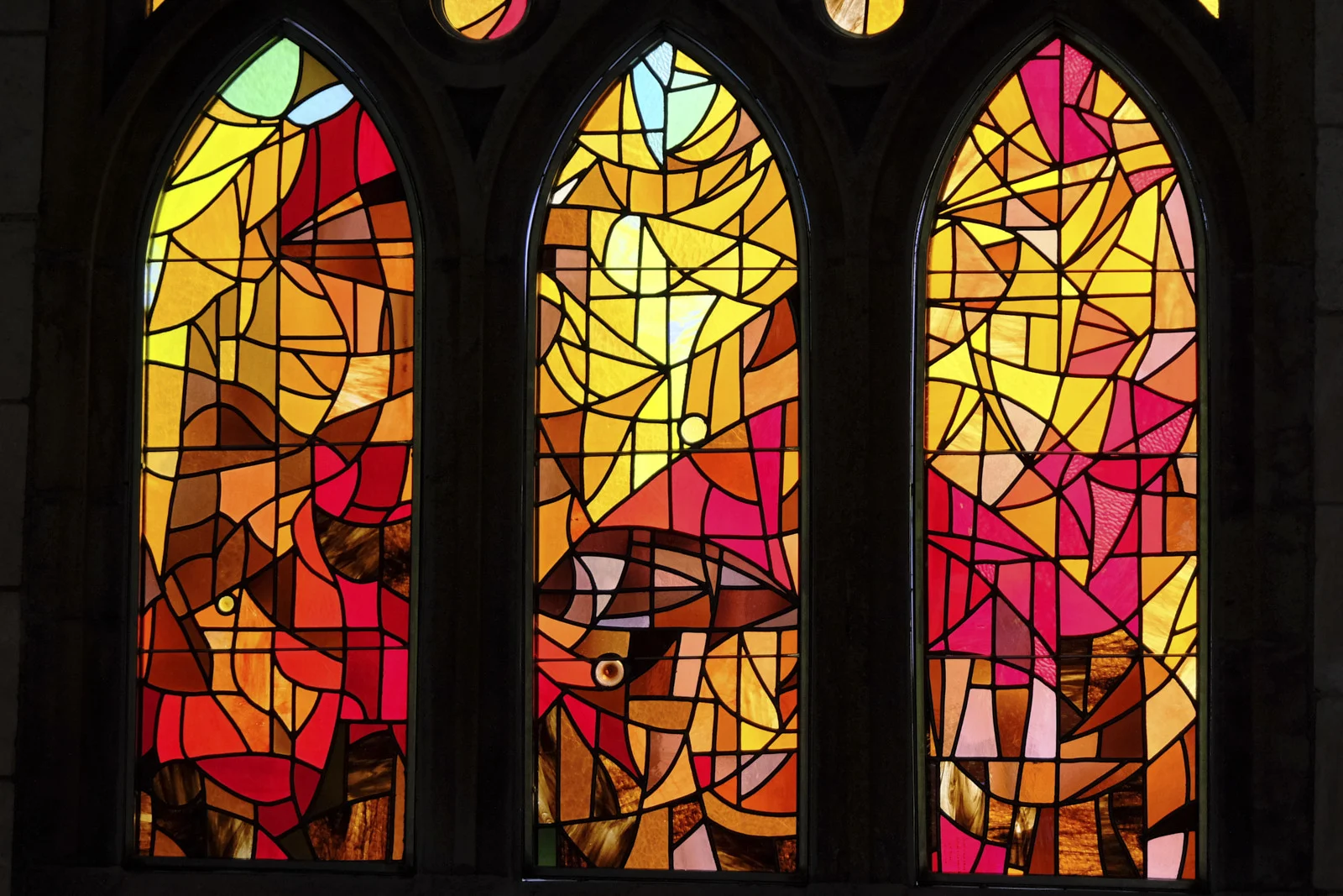 Three pointed stained-glass windows with red, orange, and yellow abstract glass in the Sagrada Família in Barcelona.