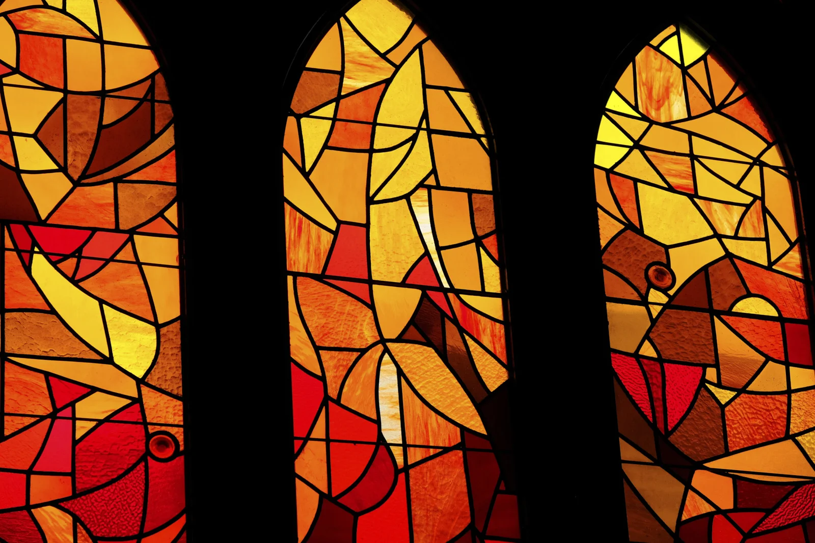 A close view of three arched stained-glass panes in red, orange, and yellow glass at the Sagrada Família in Barcelona.