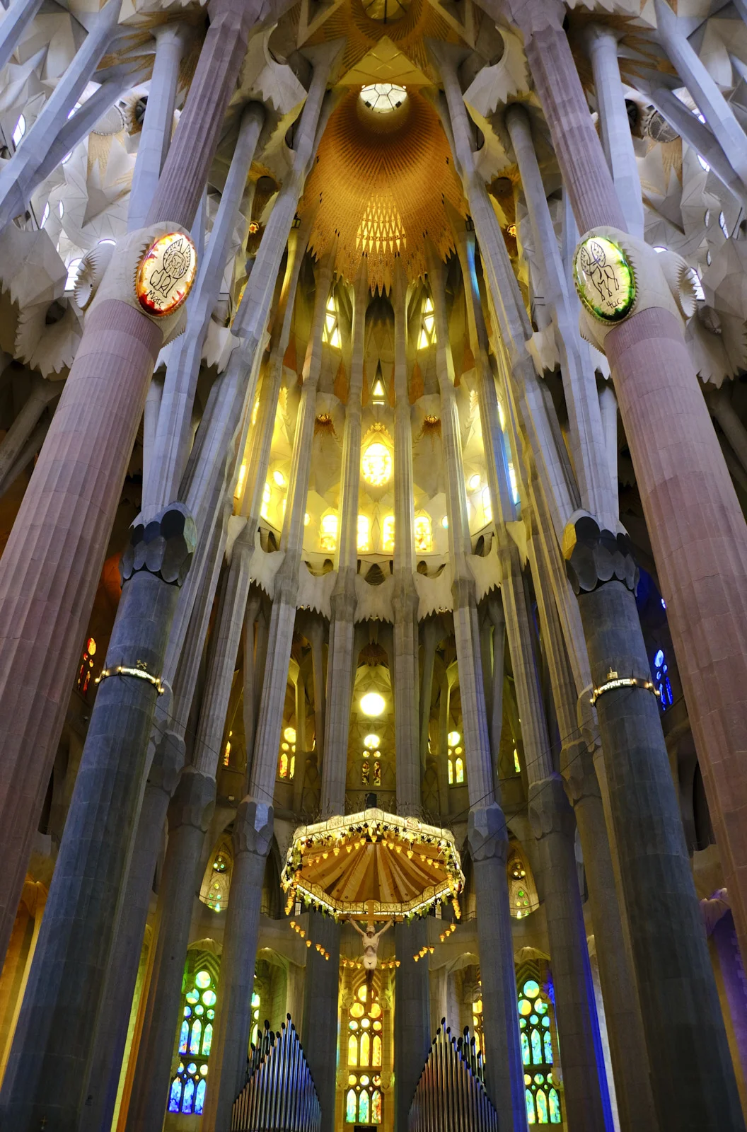 The suspended crucifix and canopy over the altar of the Sagrada Família in Barcelona, with organ pipes below and columns on either side.