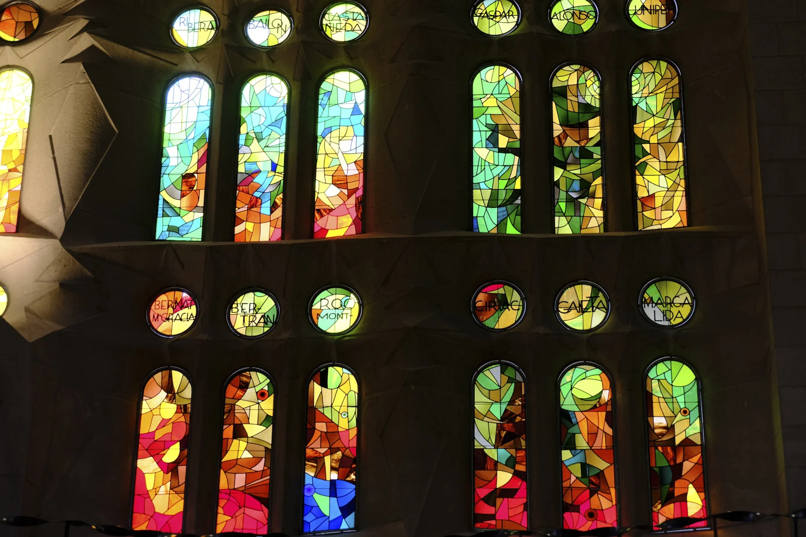 Stained-glass lancets and round windows inscribed with names in the nave of the Sagrada Família in Barcelona.