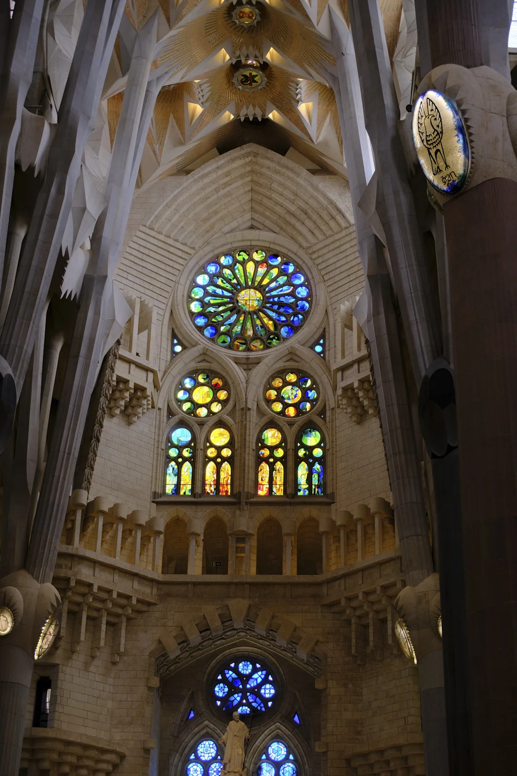 A large rose window, smaller stained-glass windows, and a statue of a bearded robed man on the Nativity facade inside the Sagrada Família in Barcelona.