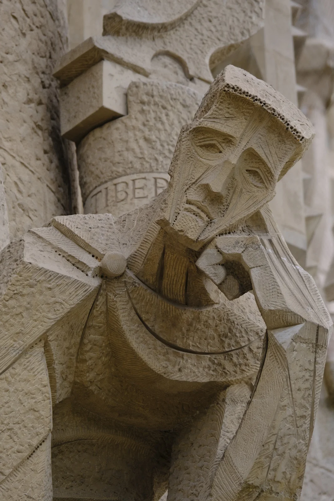 A stone figure in front of the column marked Tiberius on the Passion facade of the Sagrada Família in Barcelona.