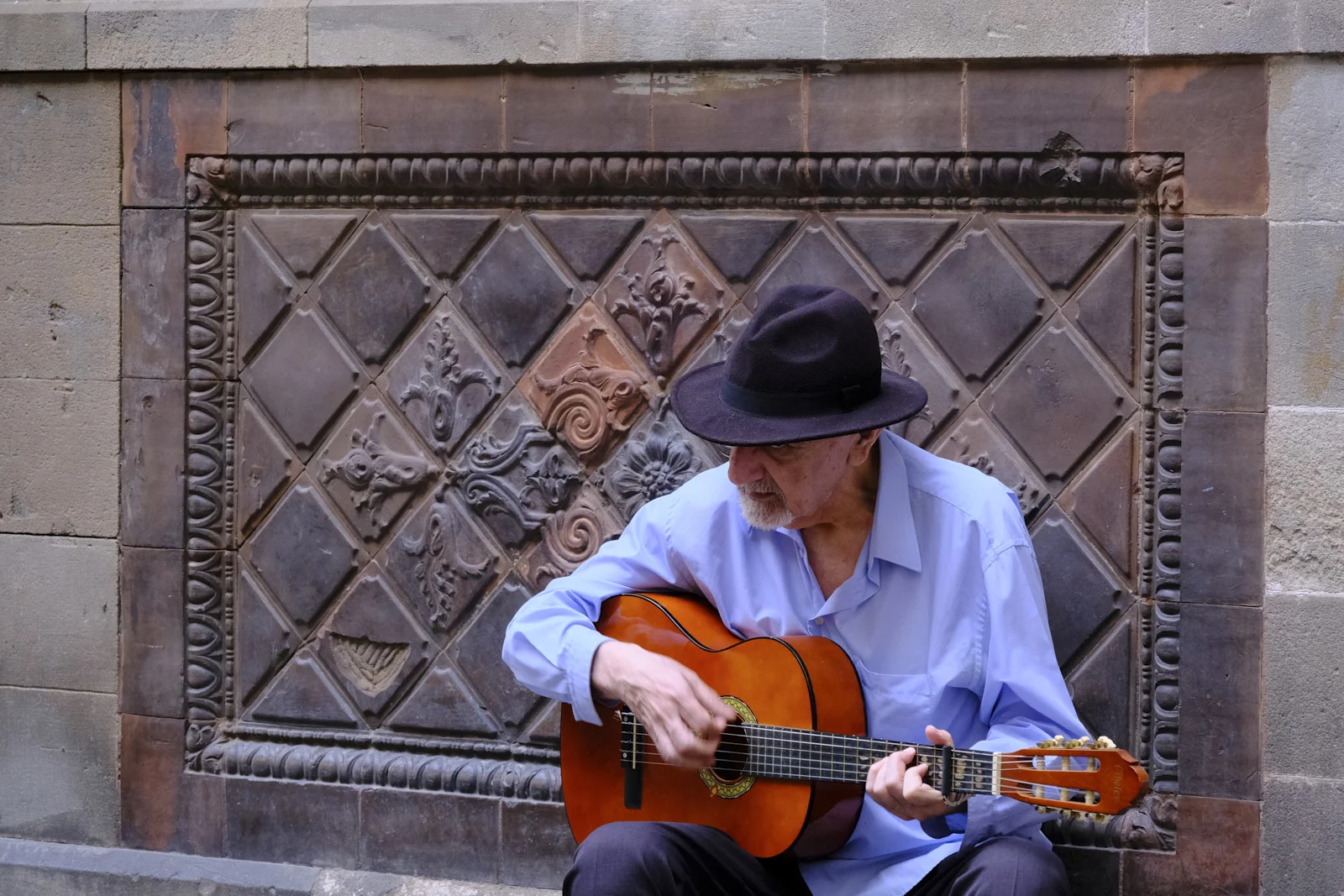 A man playing a guitar against a tiled wall in El Born, Barcelona.
