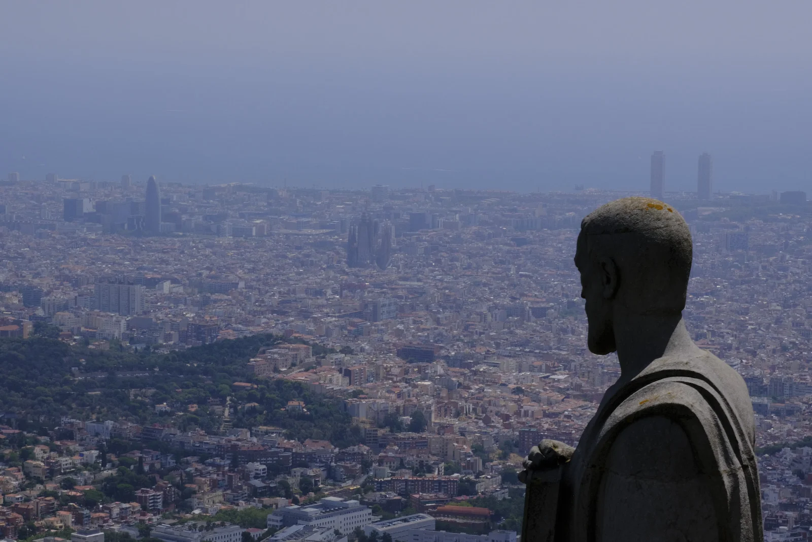A stone apostle at the Sagrat Cor on Tibidabo, overlooking Barcelona, the Sagrada Família, and the port towers.