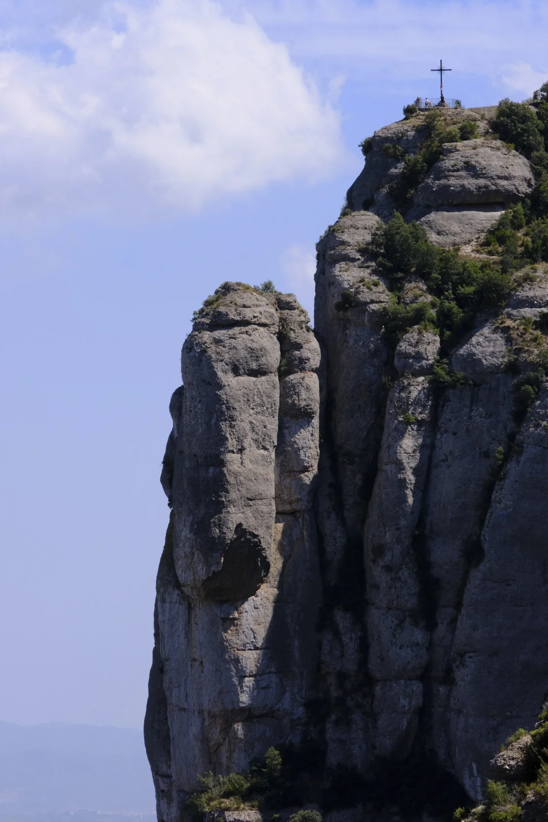 A metal cross and viewing rail on a rock summit at Montserrat, with a separate rock pillar beside the peak.