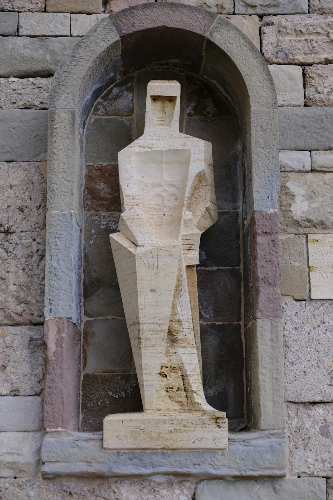 A geometric stone statue of Sant Jordi, sword and shield in hand, set in an arched niche at the monastery of Montserrat.