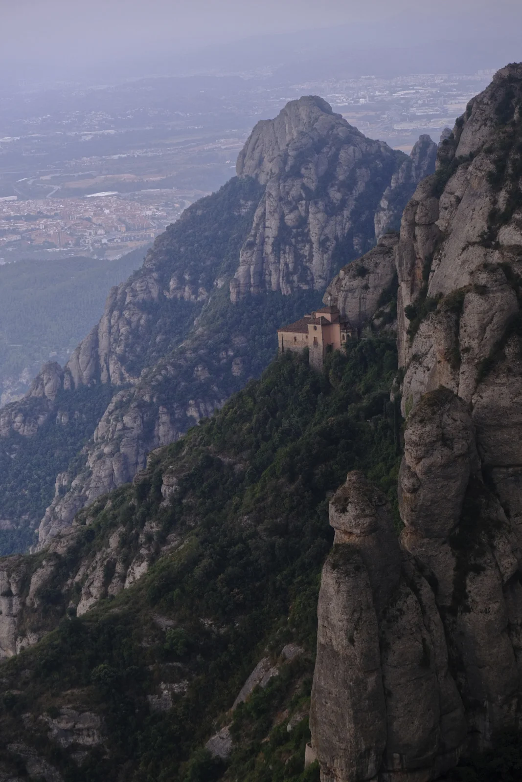 A hermitage with a tile roof on a wooded ledge of the cliff at Montserrat.