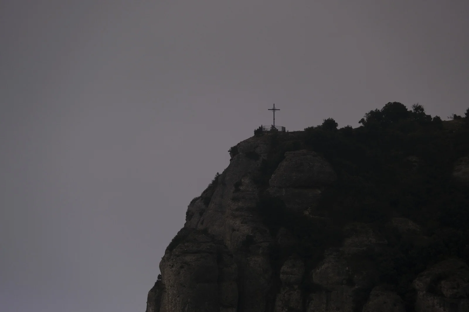 A metal cross and railing on a rocky ridge at Montserrat.