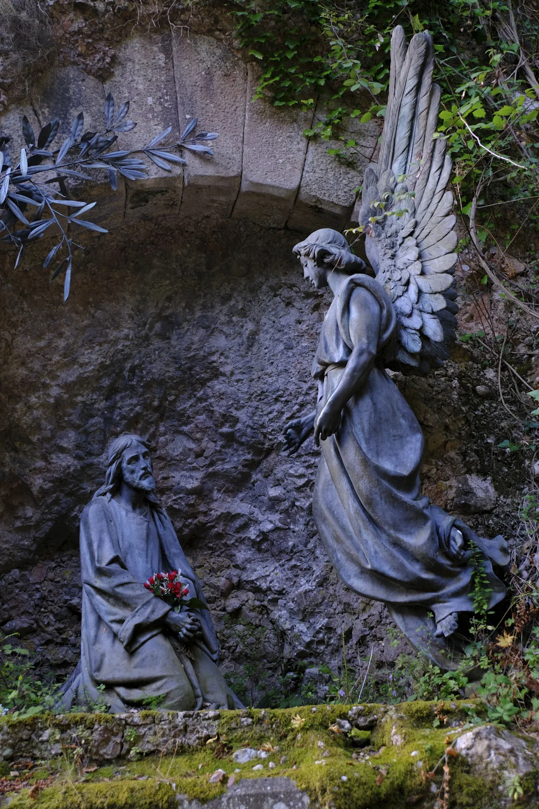 Sculptures of the kneeling Christ and a standing angel in a rock grotto on the Monumental Rosary path at Montserrat.