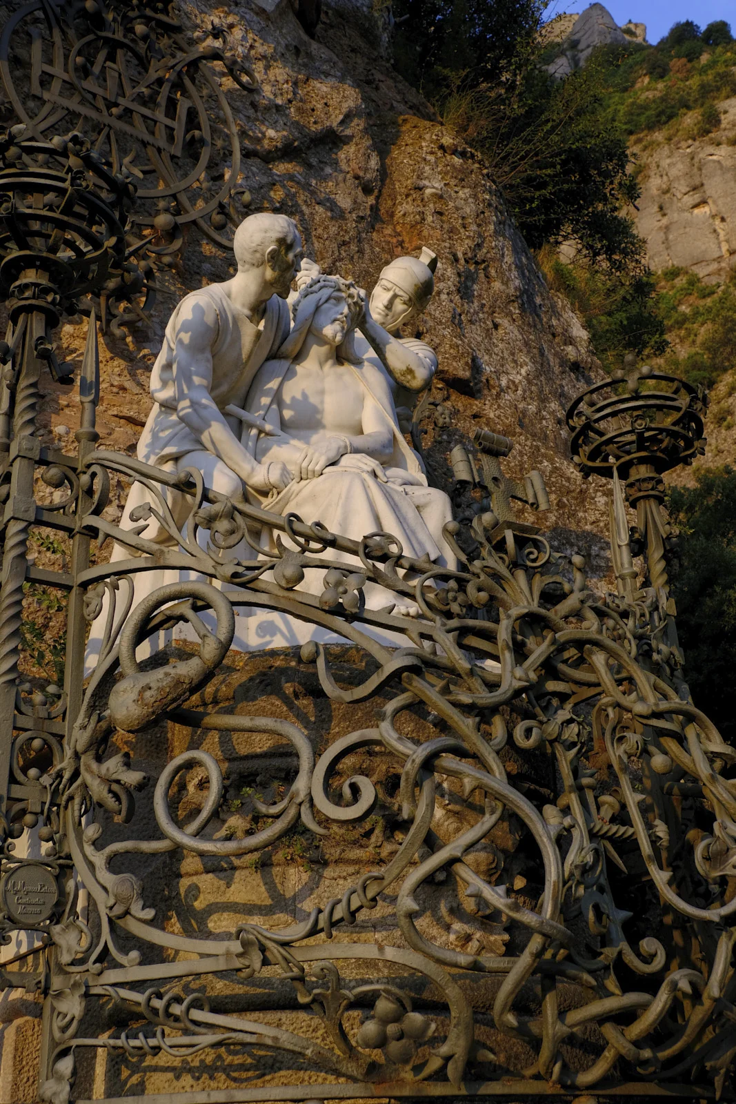 A sculpture of the seated Christ crowned with thorns, behind an iron screen, on the Monumental Rosary path at Montserrat.