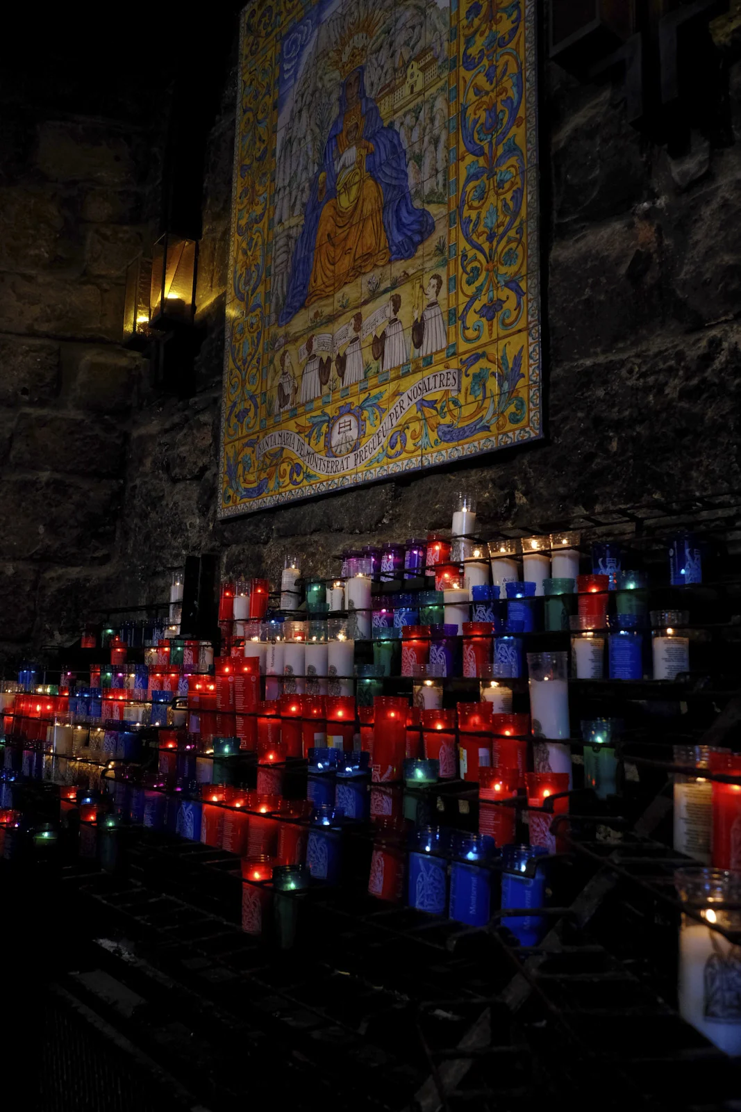 Racks of votive candles before a ceramic tile of Santa Maria de Montserrat in the basilica at Montserrat.