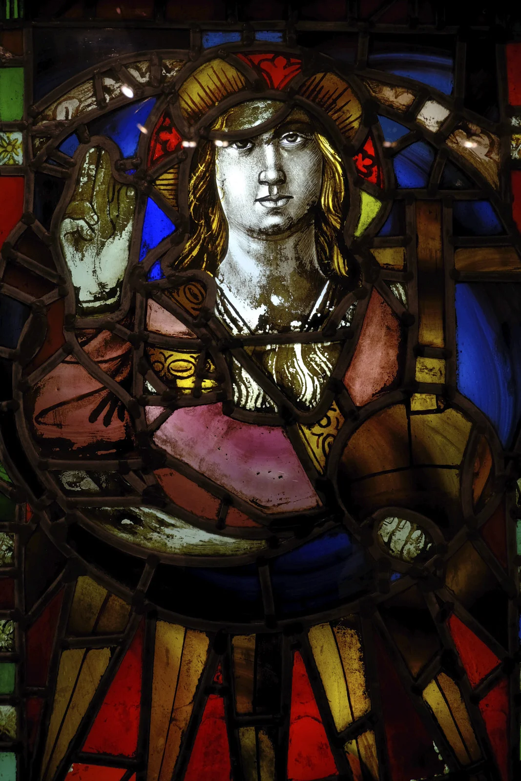 A stained-glass window in the basilica at Montserrat with a haloed figure, one hand raised, and a cross beside the figure.