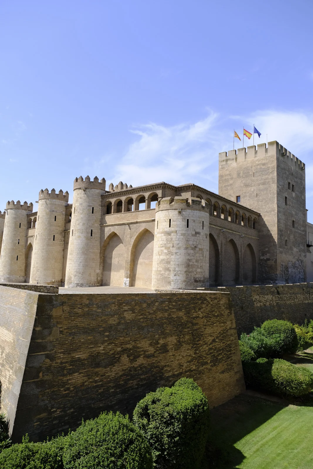 The square Torre del Trovador of the Aljafería Palace in Zaragoza rises beside round towers above a brick rampart.