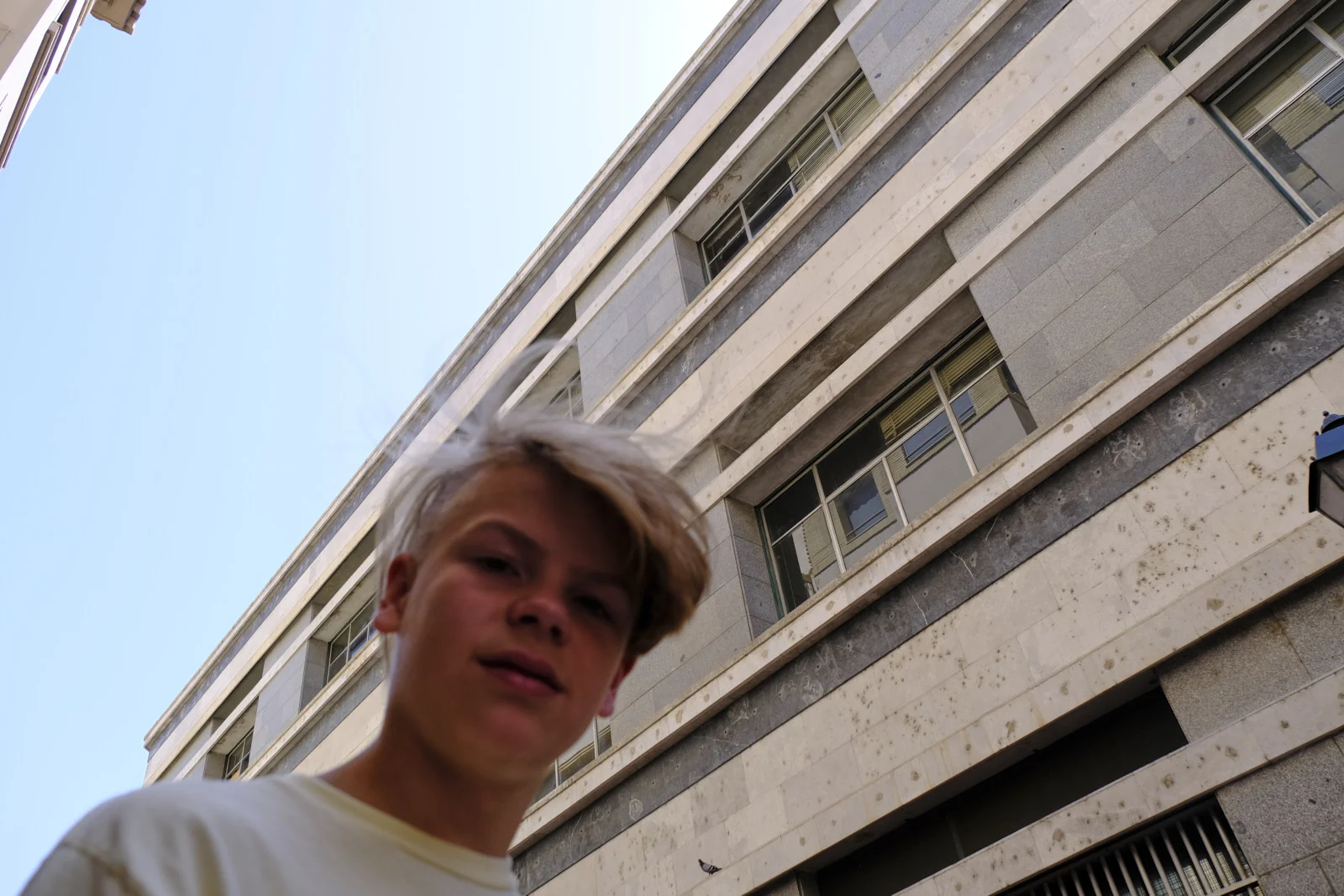 A boy faces the camera on Calle José Palafox in Zaragoza, with a stone building behind him.