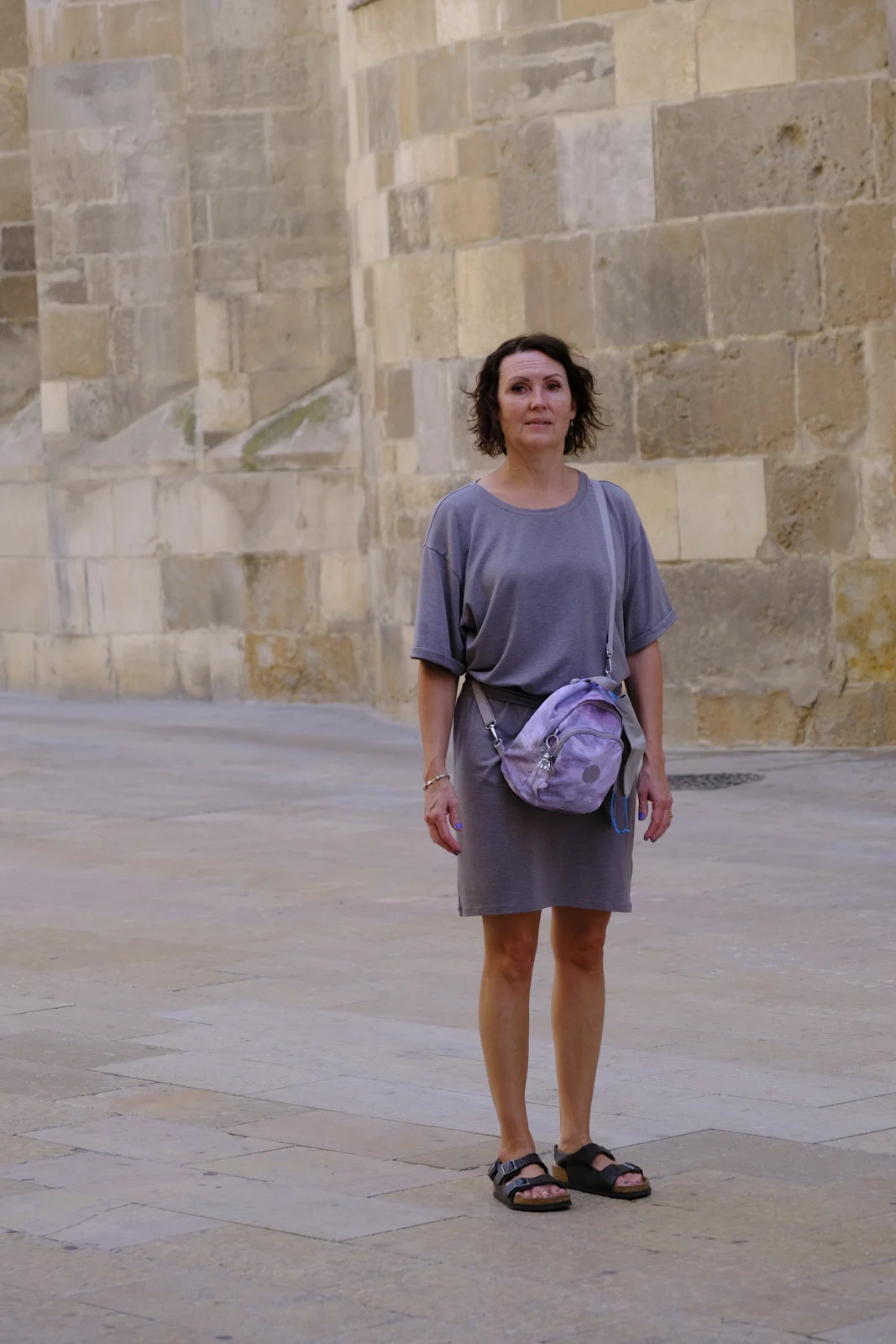 A woman stands on the paving before a large ashlar wall of La Seo in Zaragoza.