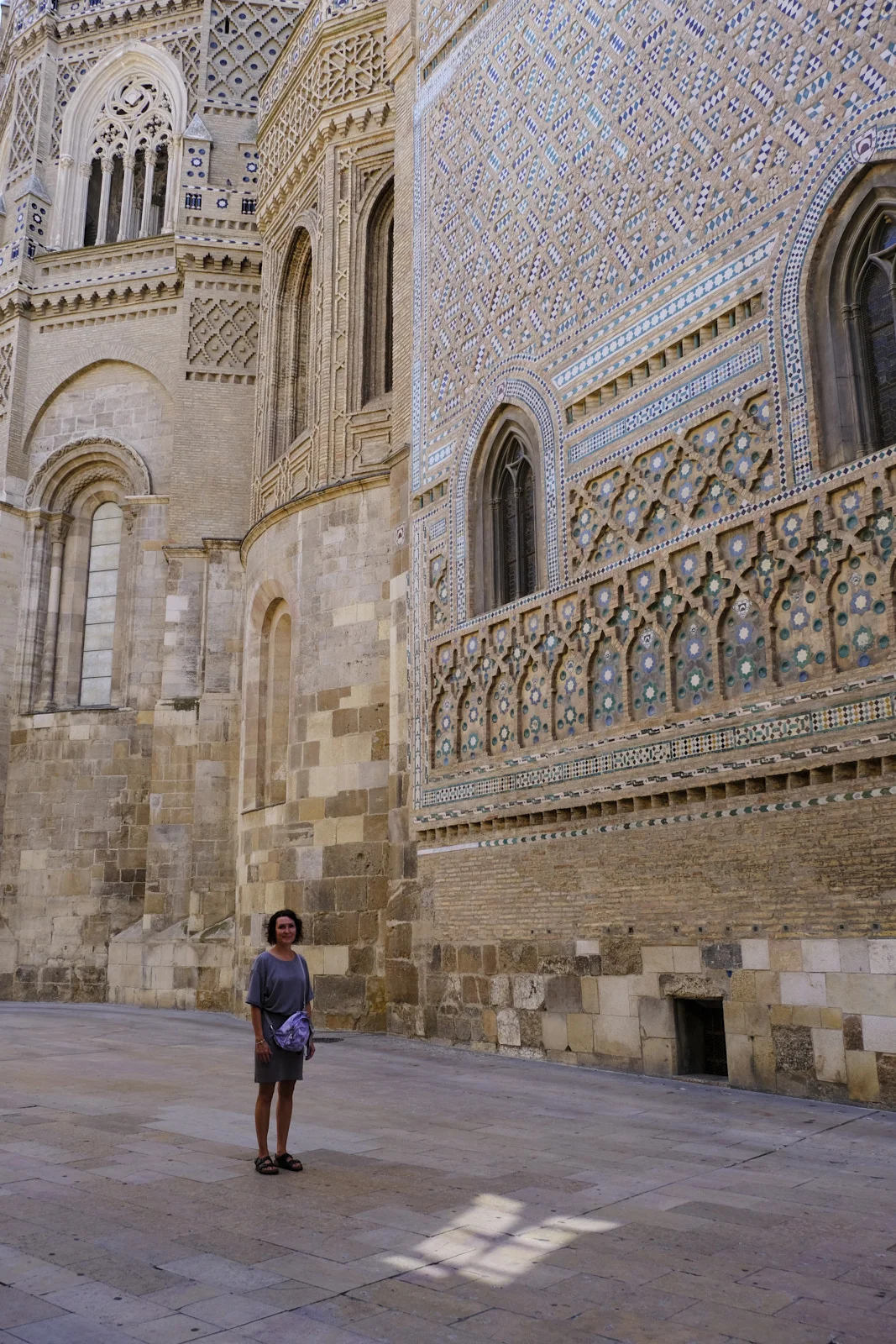 A woman stands before the Mudéjar wall of the Parroquieta and the stone apse of La Seo in Zaragoza.