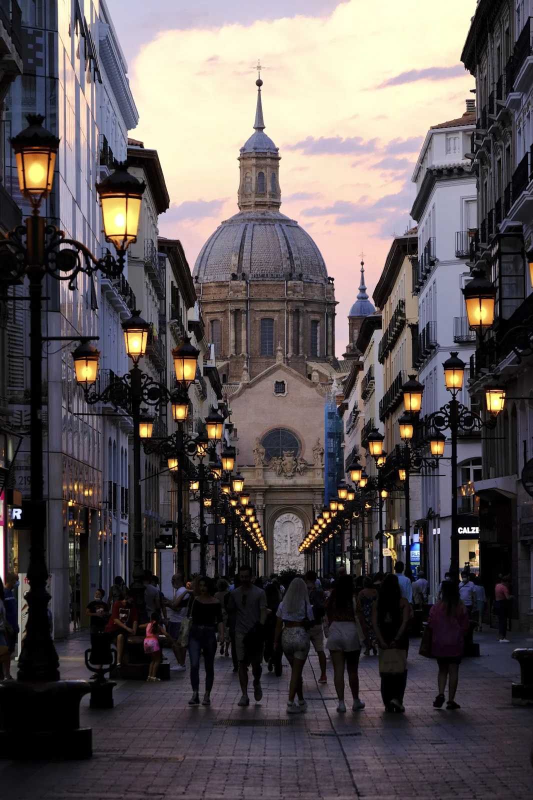 Pedestrians walk down Calle Alfonso I in Zaragoza toward the dome of the Basilica of Our Lady of the Pillar.