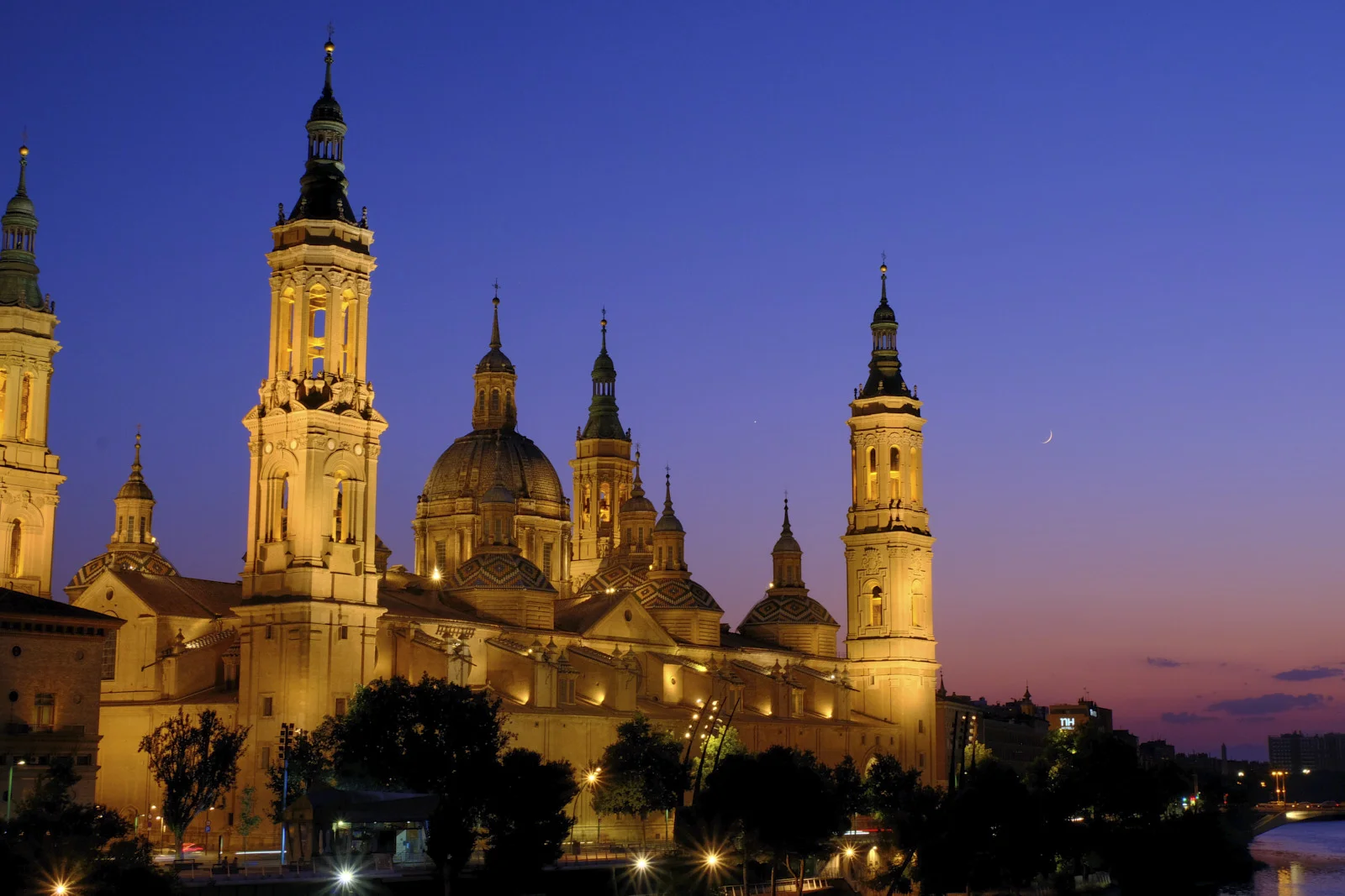 The corner towers, central dome, and smaller cupolas of the Basilica of Our Lady of the Pillar in Zaragoza, with the Ebro at the lower right.