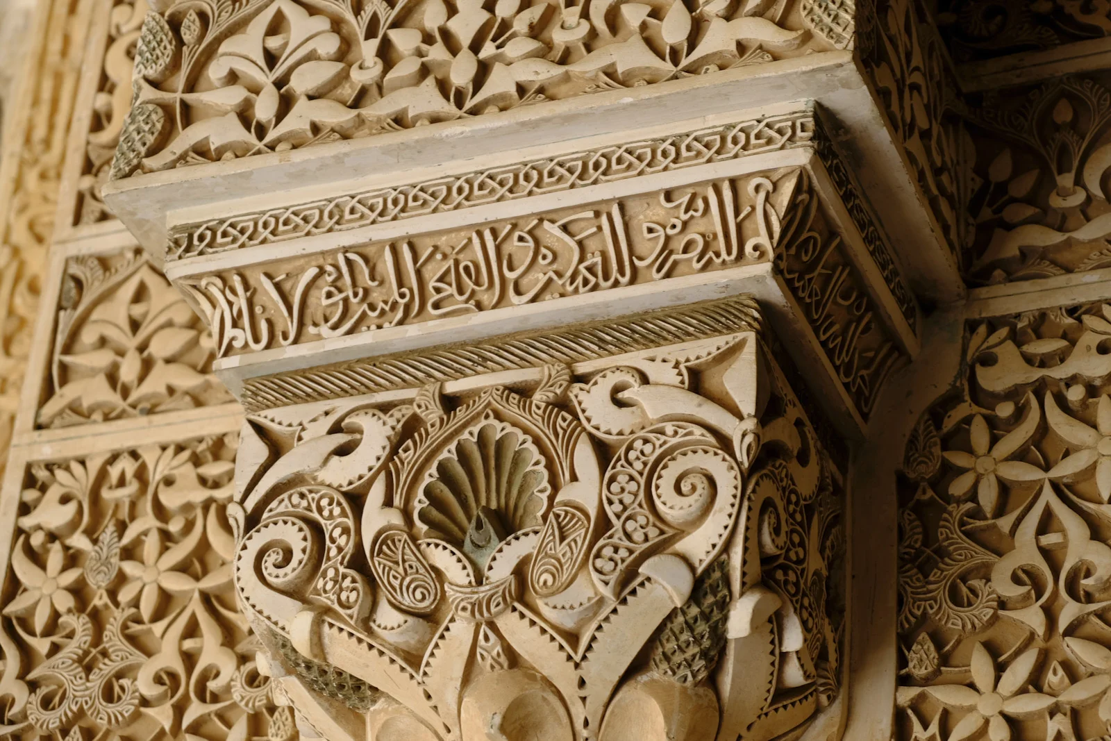 A Nasrid capital with a shell motif, plant scrolls, and a band of Arabic script on the abacus.