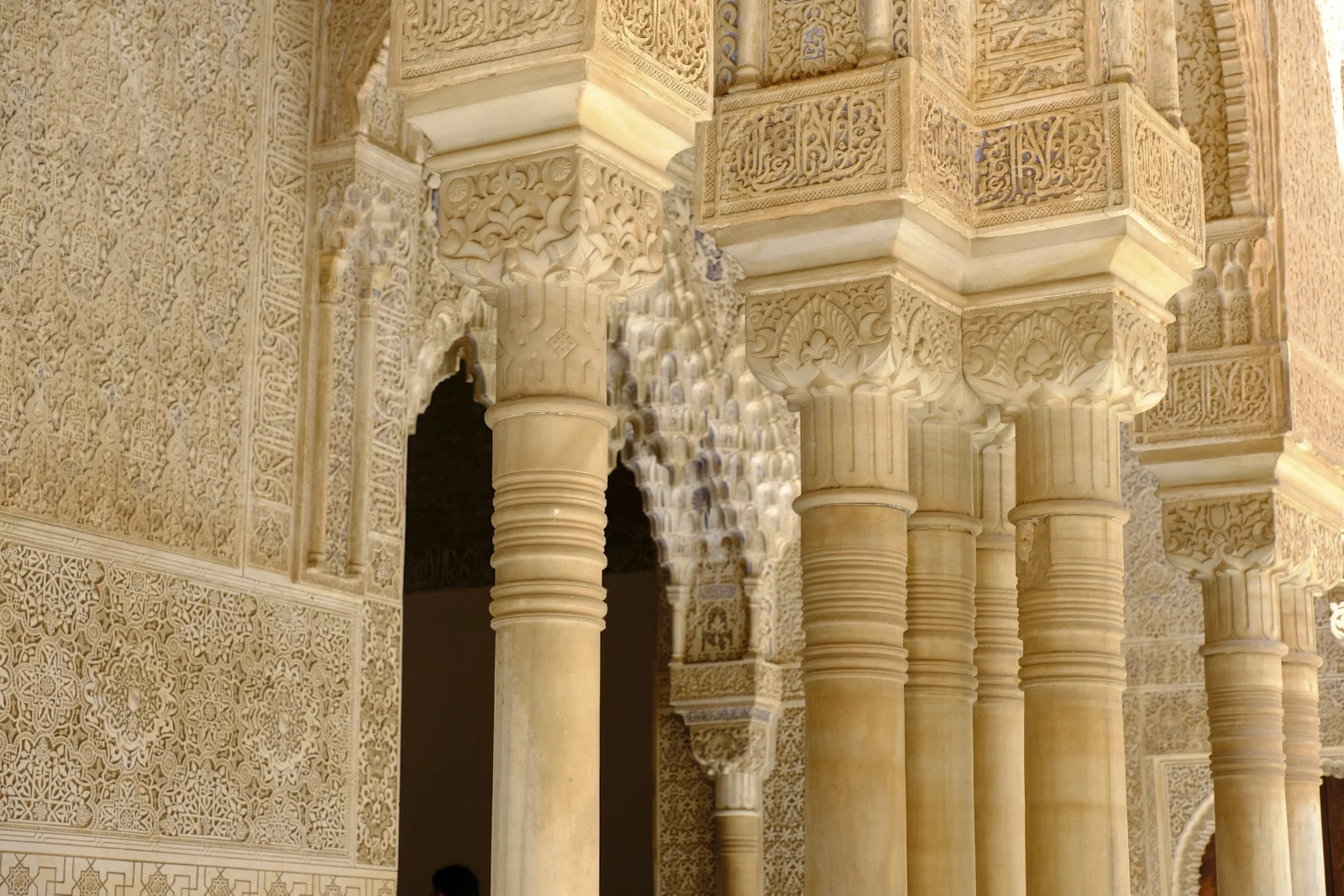 A row of slender columns with carved capitals stands in front of stucco walls and muqarnas arches.