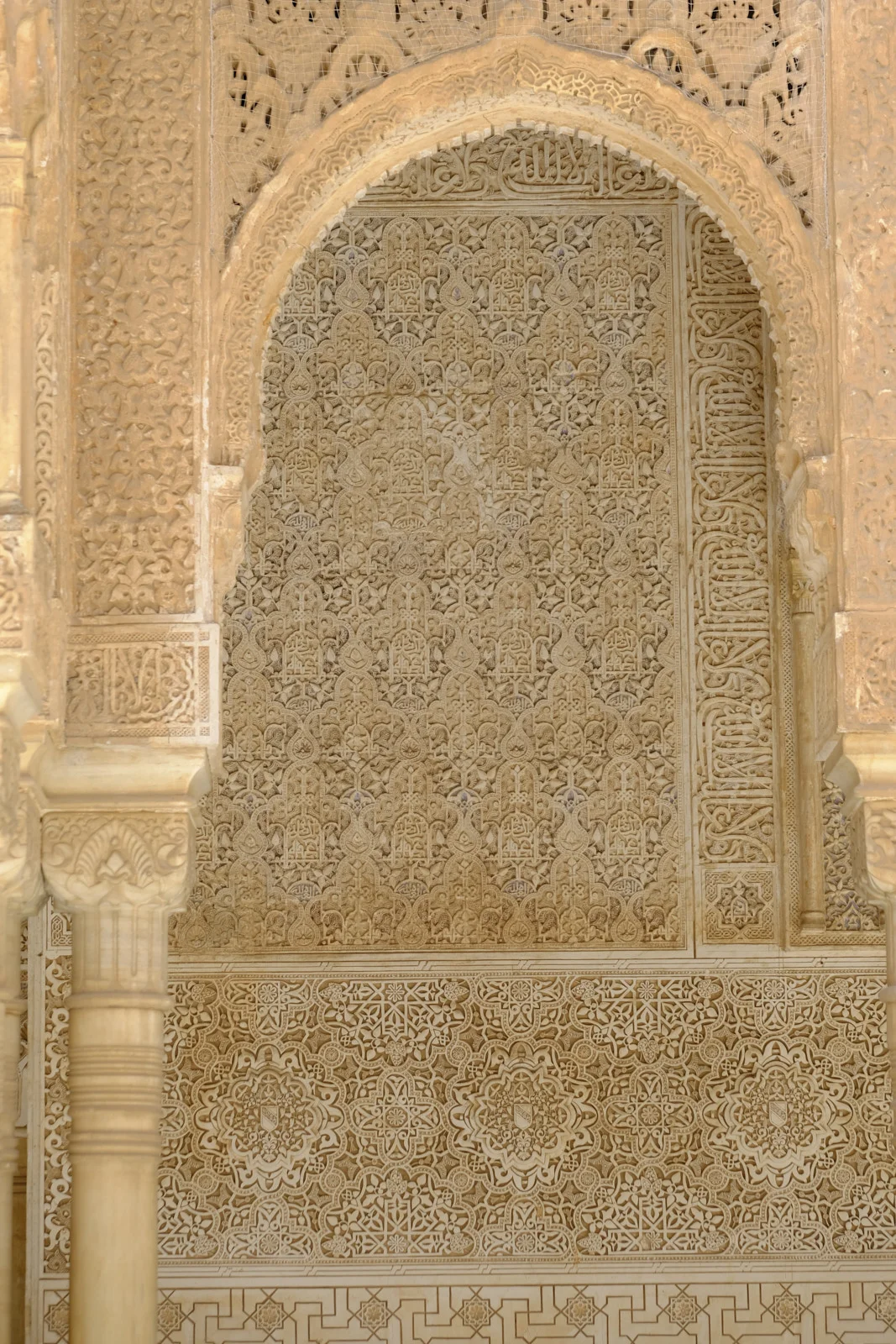 A horseshoe arch frames a panel of small carved arches above a band of eight-pointed stars, with a column at the left.
