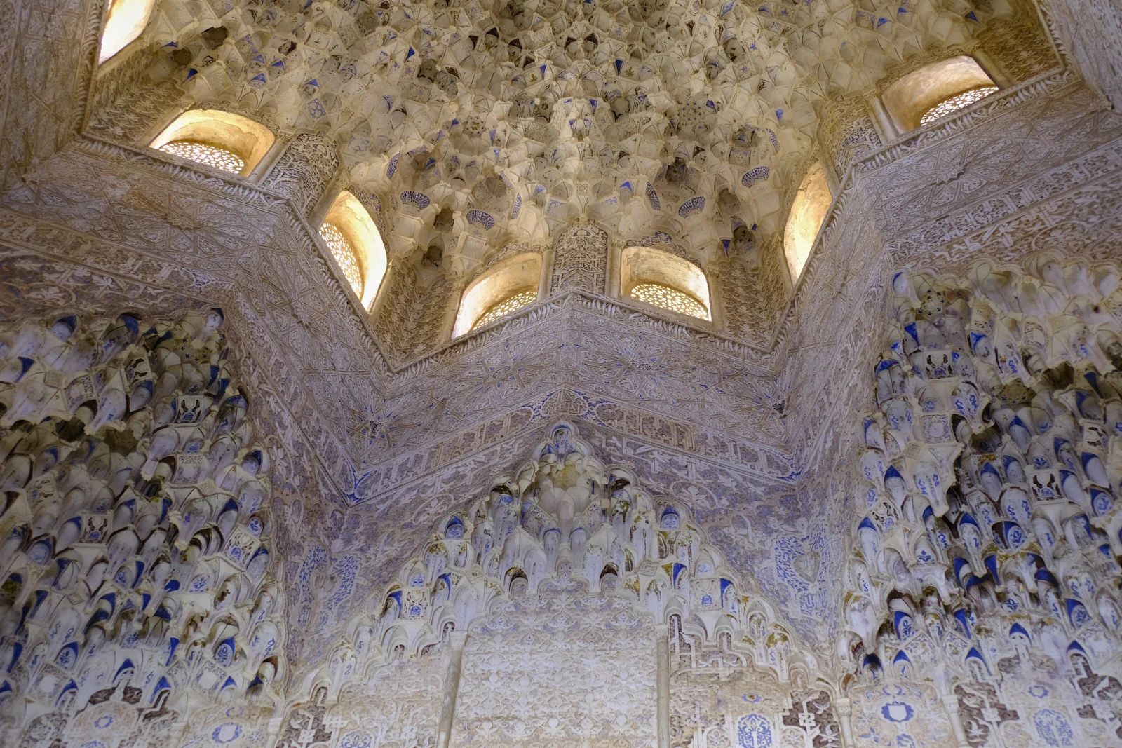 A muqarnas dome and its drum windows rise above arches of muqarnas and carved stucco walls.