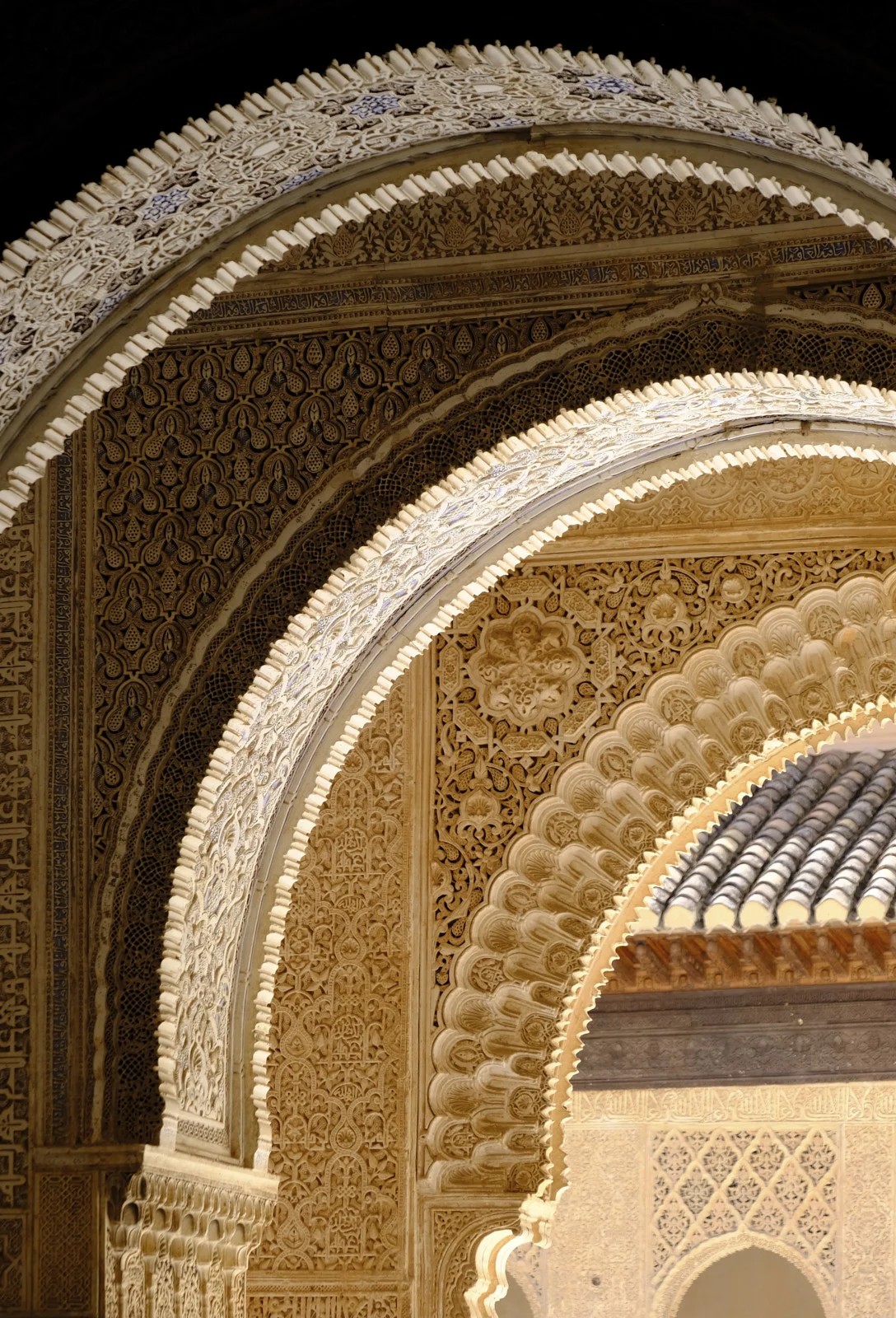 Nested horseshoe arches carved with geometric patterns and scalloped edges, with roof tiles visible through the inner arch.