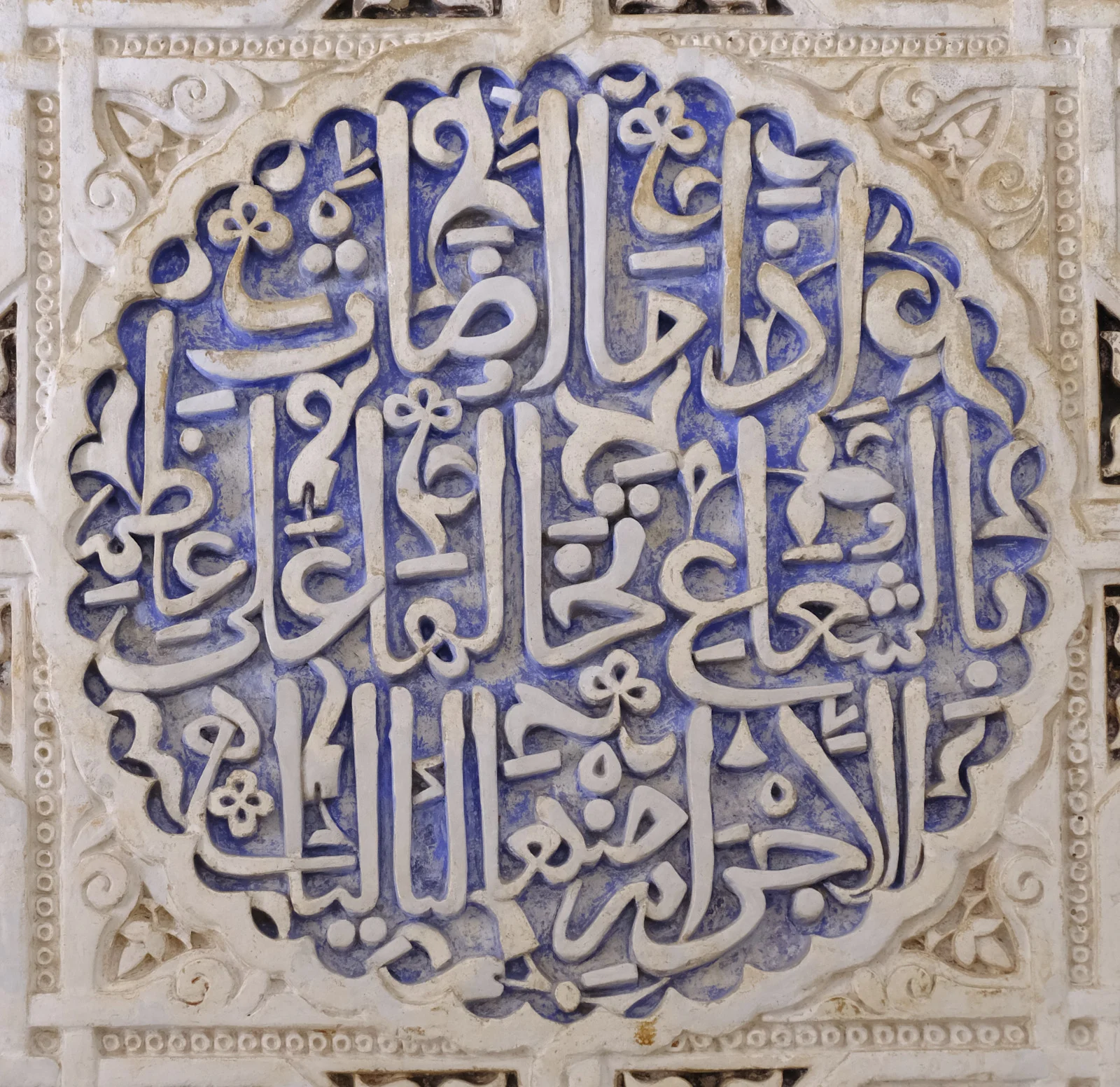 A circular medallion of carved Arabic letters set in a square stucco frame.