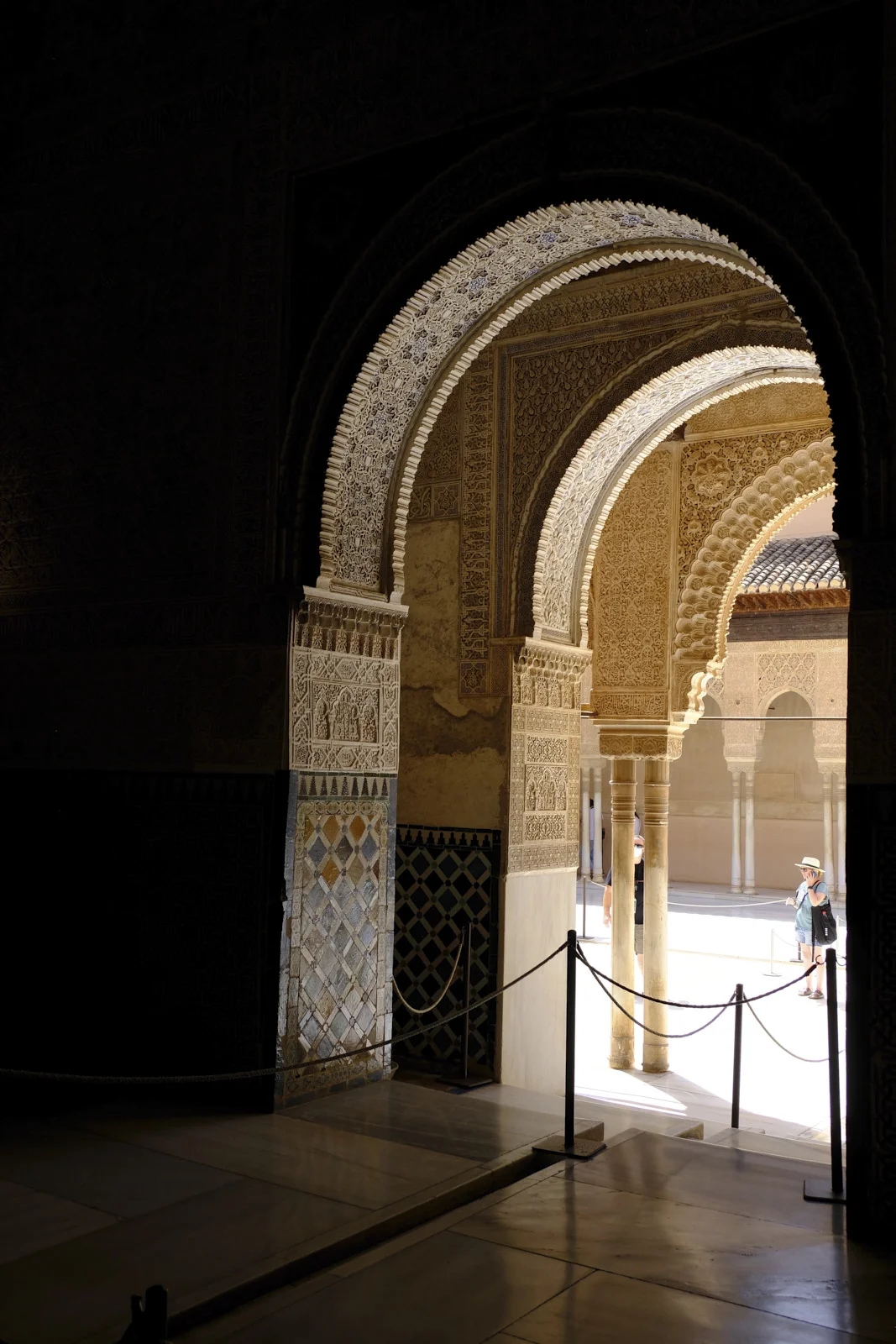 Carved horseshoe arches frame a columned courtyard and a tiled roof beyond.