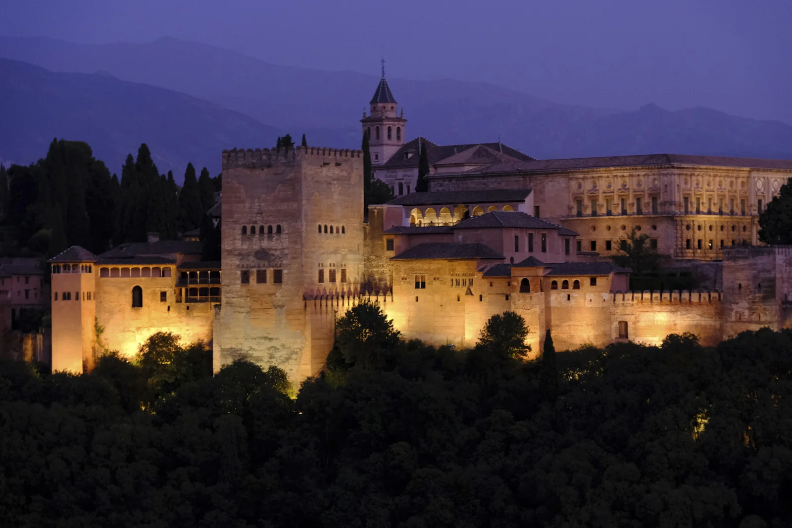 The Comares Tower stands in front of the church of Santa María, with the Palace of Charles V extending beside it, above the trees.