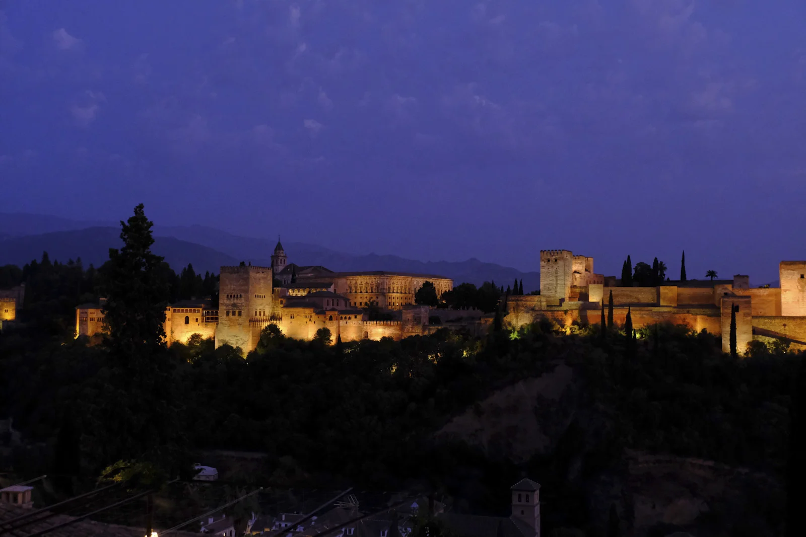 The Alhambra along the ridge, the Comares Tower and the Palace of Charles V toward the left and the Alcazaba with the Torre de la Vela toward the right, above rooftops on the Albaicín side.