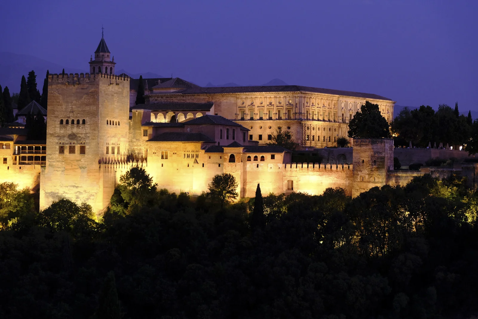 The Comares Tower and the church of Santa María stand beside the long facade of the Palace of Charles V, with a smaller wall tower at the right.