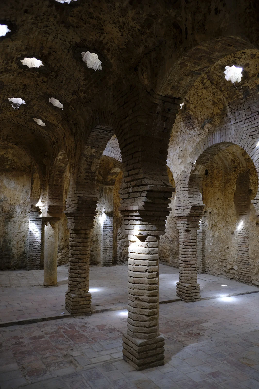 Brick columns support horseshoe arches in the Arab baths at Ronda, under a vault with star-shaped openings.