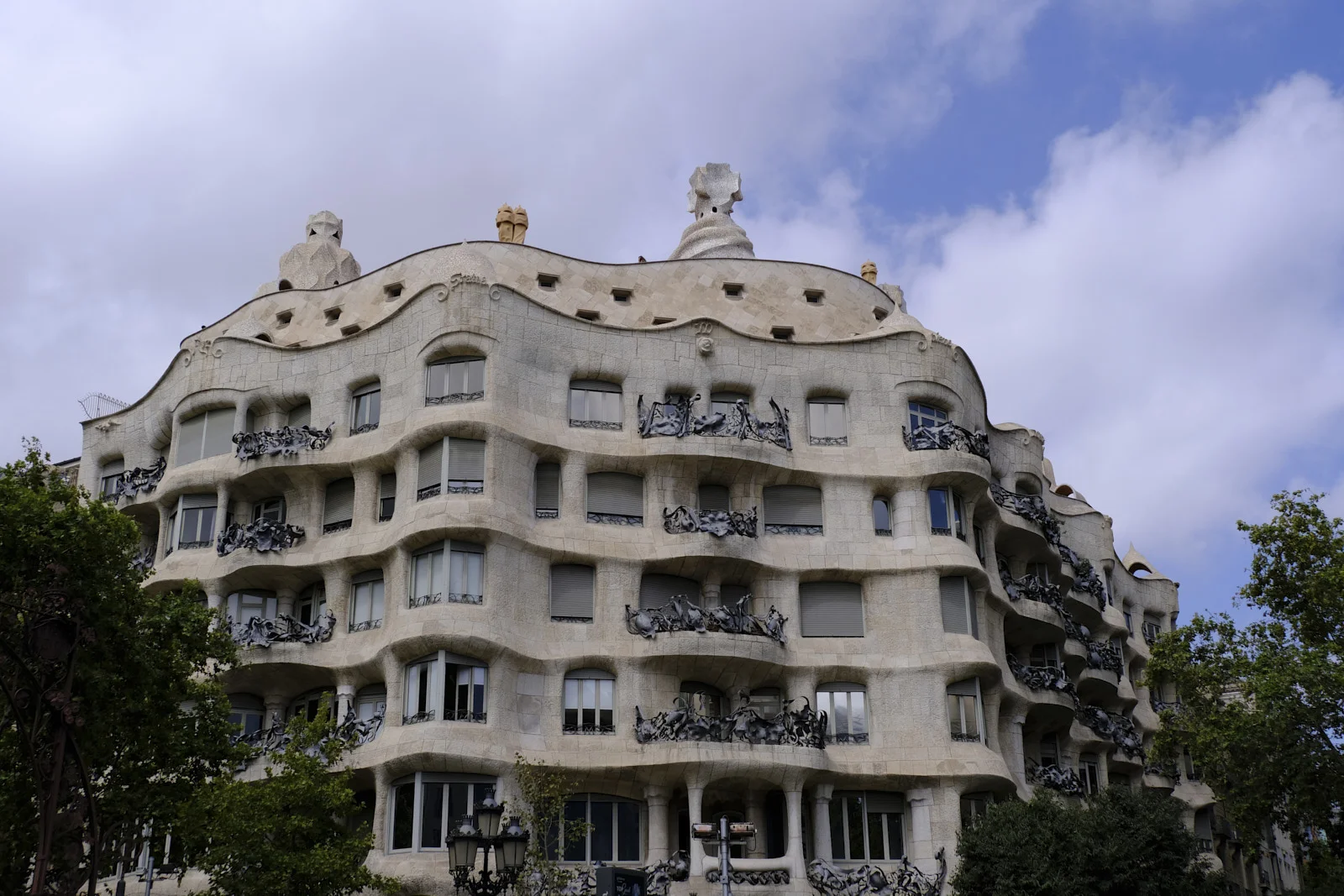 The stone facade of La Pedrera in Barcelona has wrought-iron balconies and chimney pots along the roof.