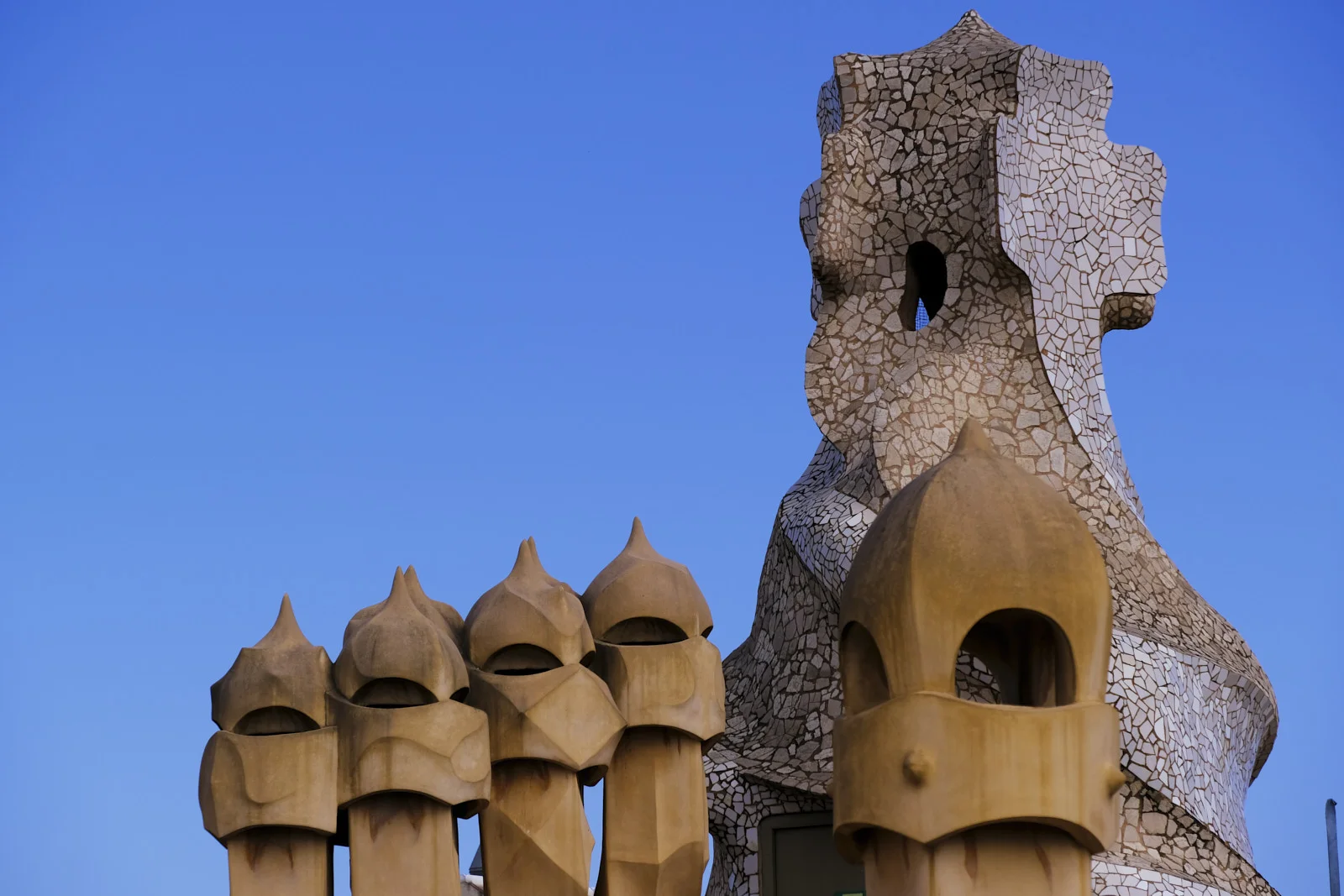 Chimney pots stand in front of a broken-tile stair tower on the roof of La Pedrera in Barcelona.