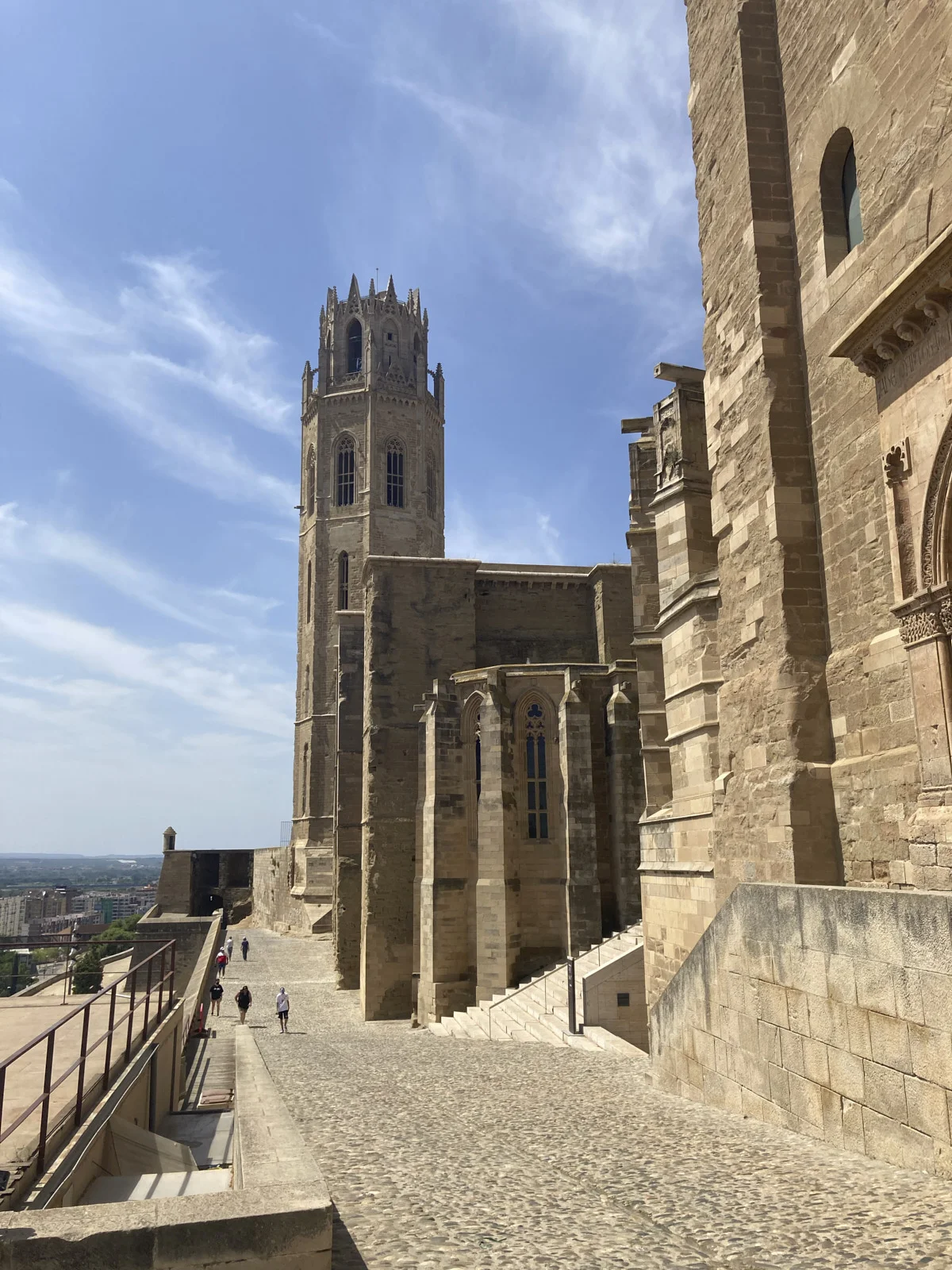 The bell tower of the Seu Vella rises beside the old cathedral in Lleida, with visitors on the cobbled walk.